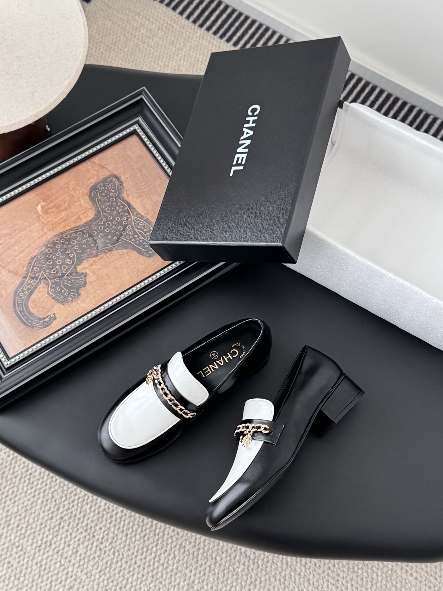 A pair of Chanel black and white leather loafers with gold-tone chain and CC logo sitting next to a Chanel shoe box. - Hình 3