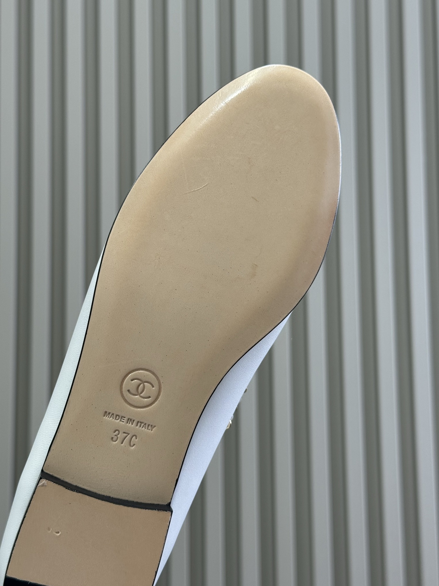 A pair of Chanel white leather ballet flats with black patent toe caps and gold chain detailing resting on a black designer box. - Hình 6