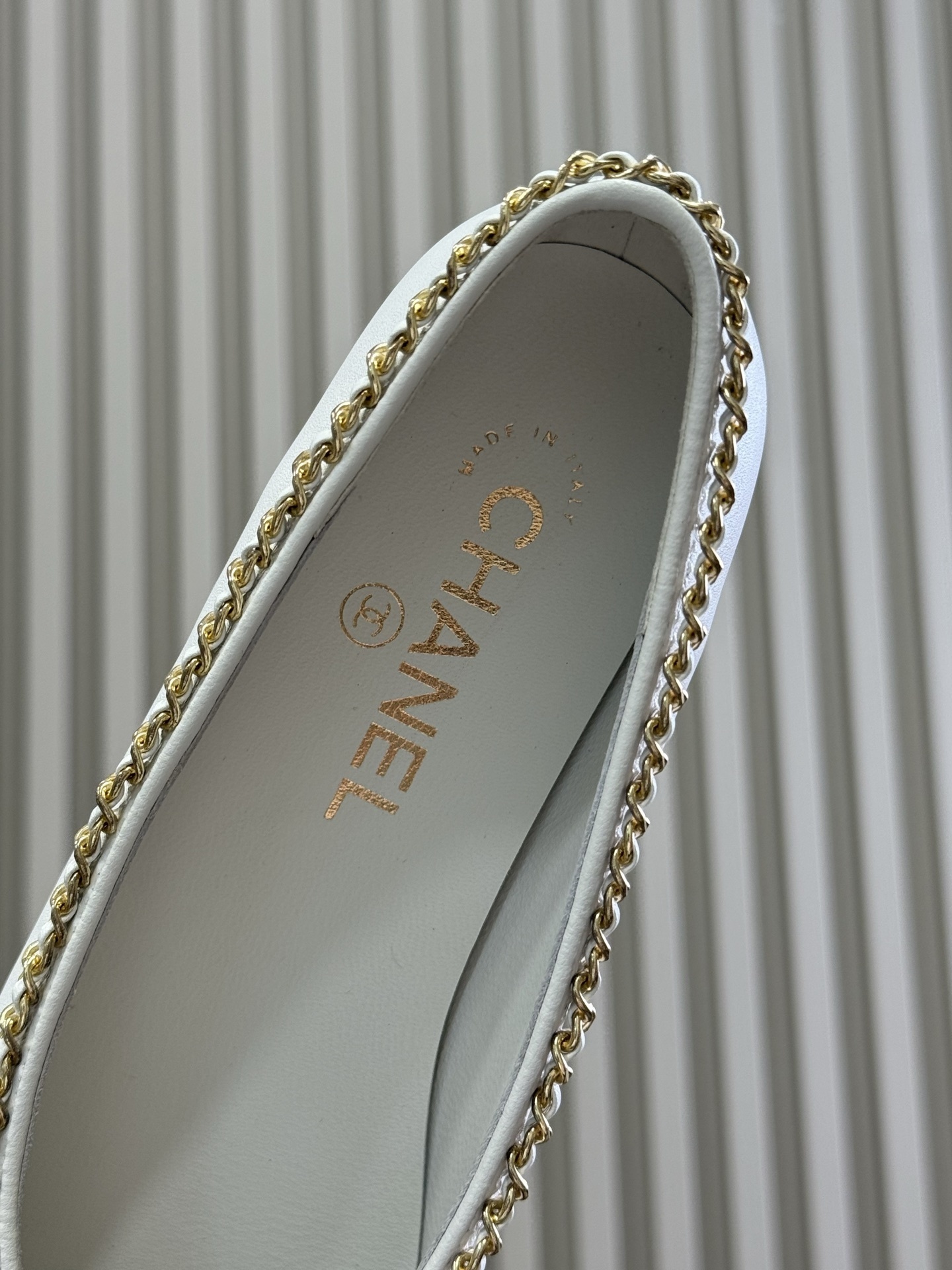 A pair of Chanel white leather ballet flats with black patent toe caps and gold chain detailing resting on a black designer box. - Hình 5
