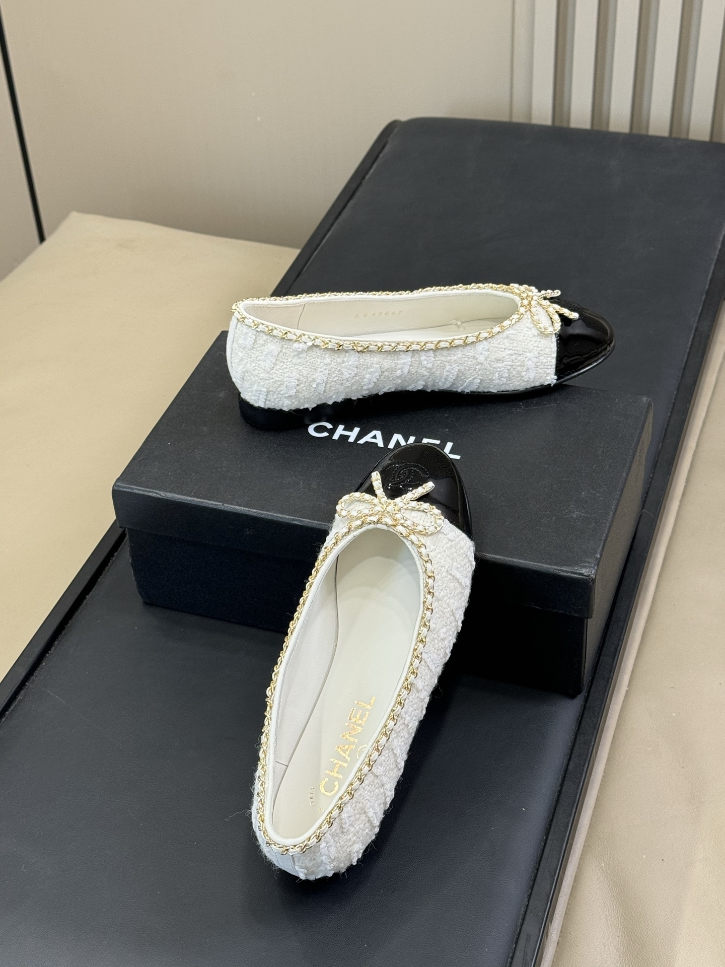 Luxury Chanel ballet flats made of white tweed and black patent leather with gold chain trim and bow detail on a black box. - Hình 4