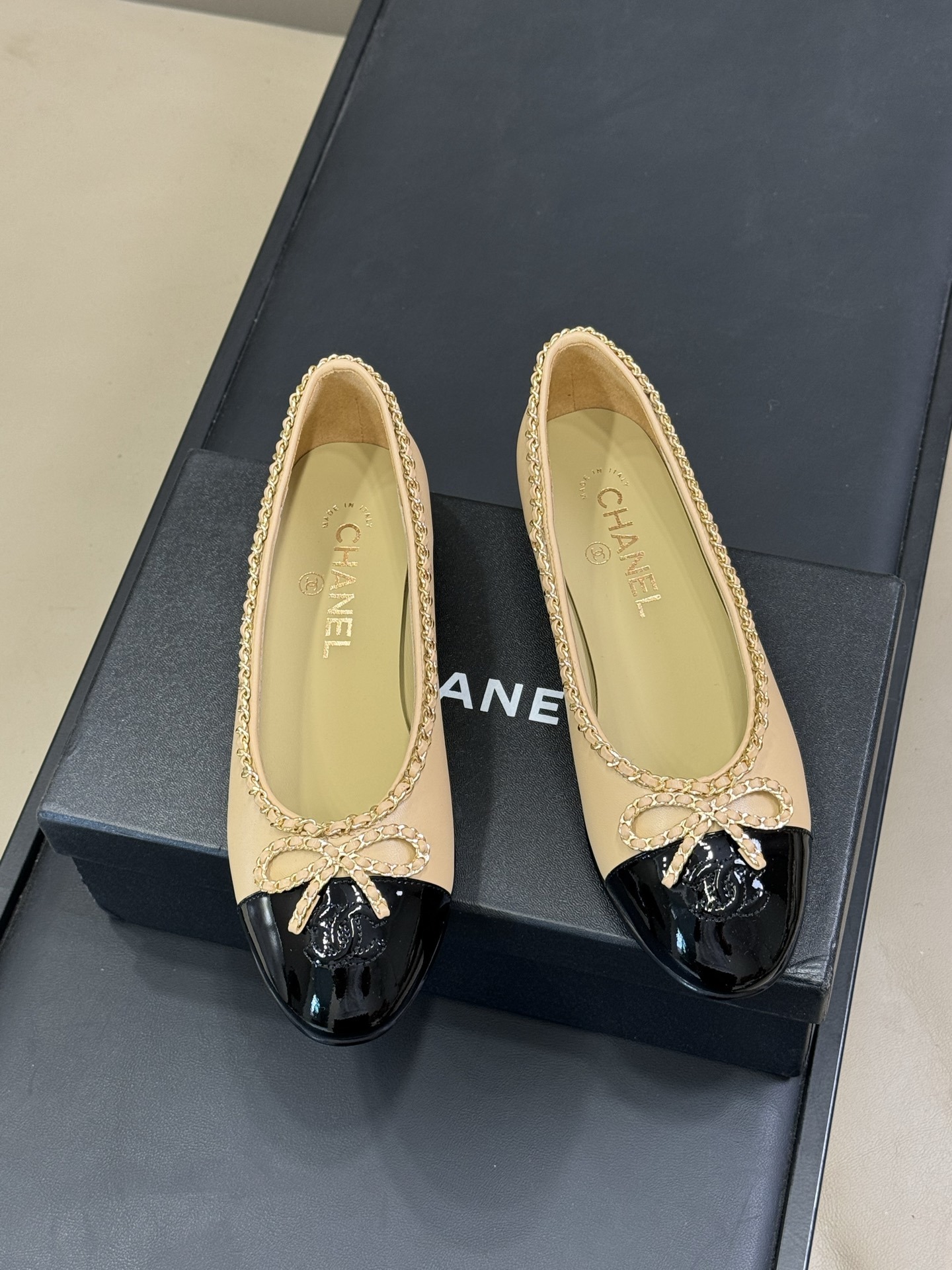 Pair of luxury beige leather ballet flats with black patent leather cap toes and gold chain link bow detailing - Hình 2