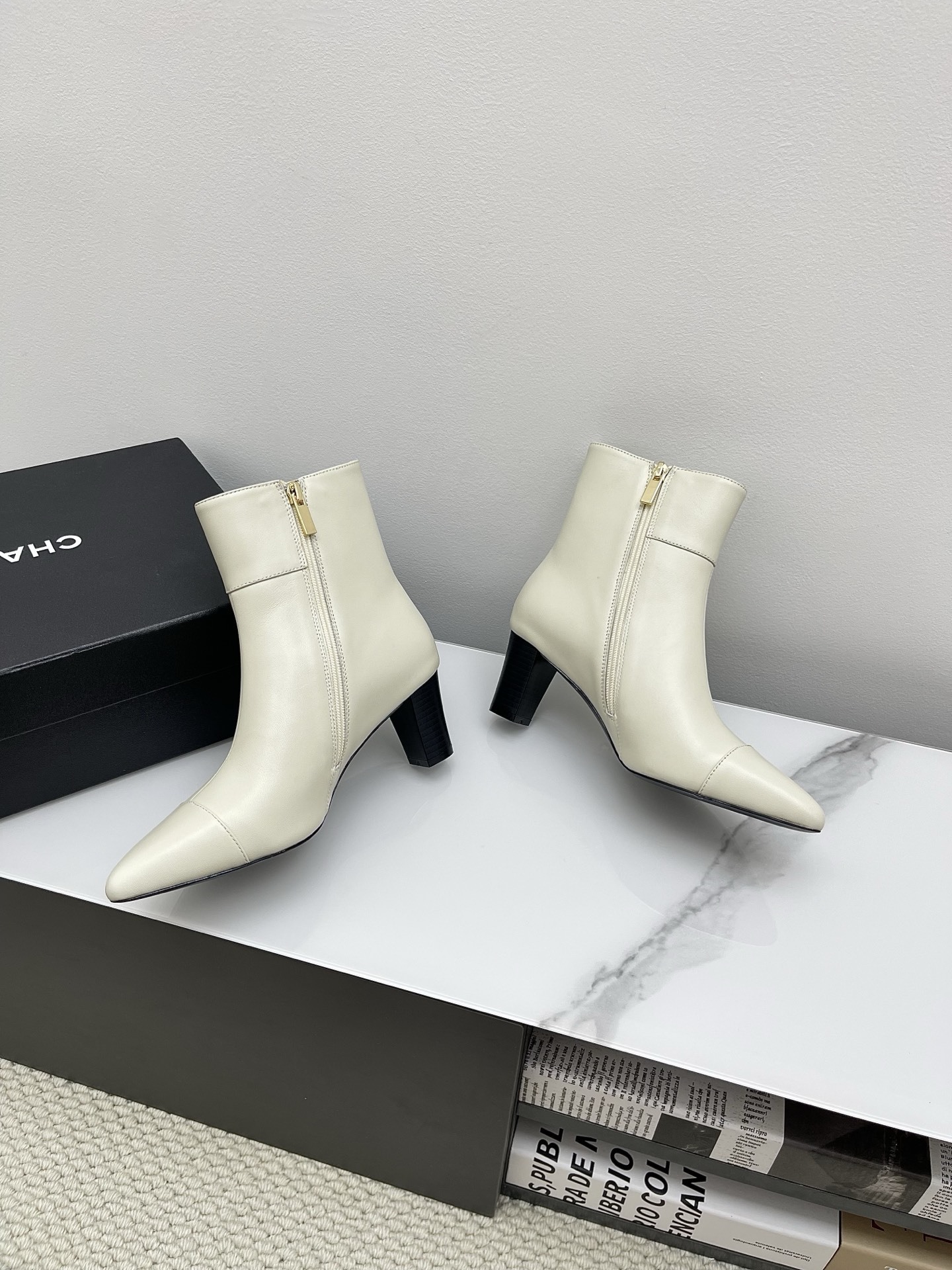 Pair of Chanel ivory leather pointed-toe ankle boots with gold lion head emblem and side zipper on a white marble surface. - Hình 9