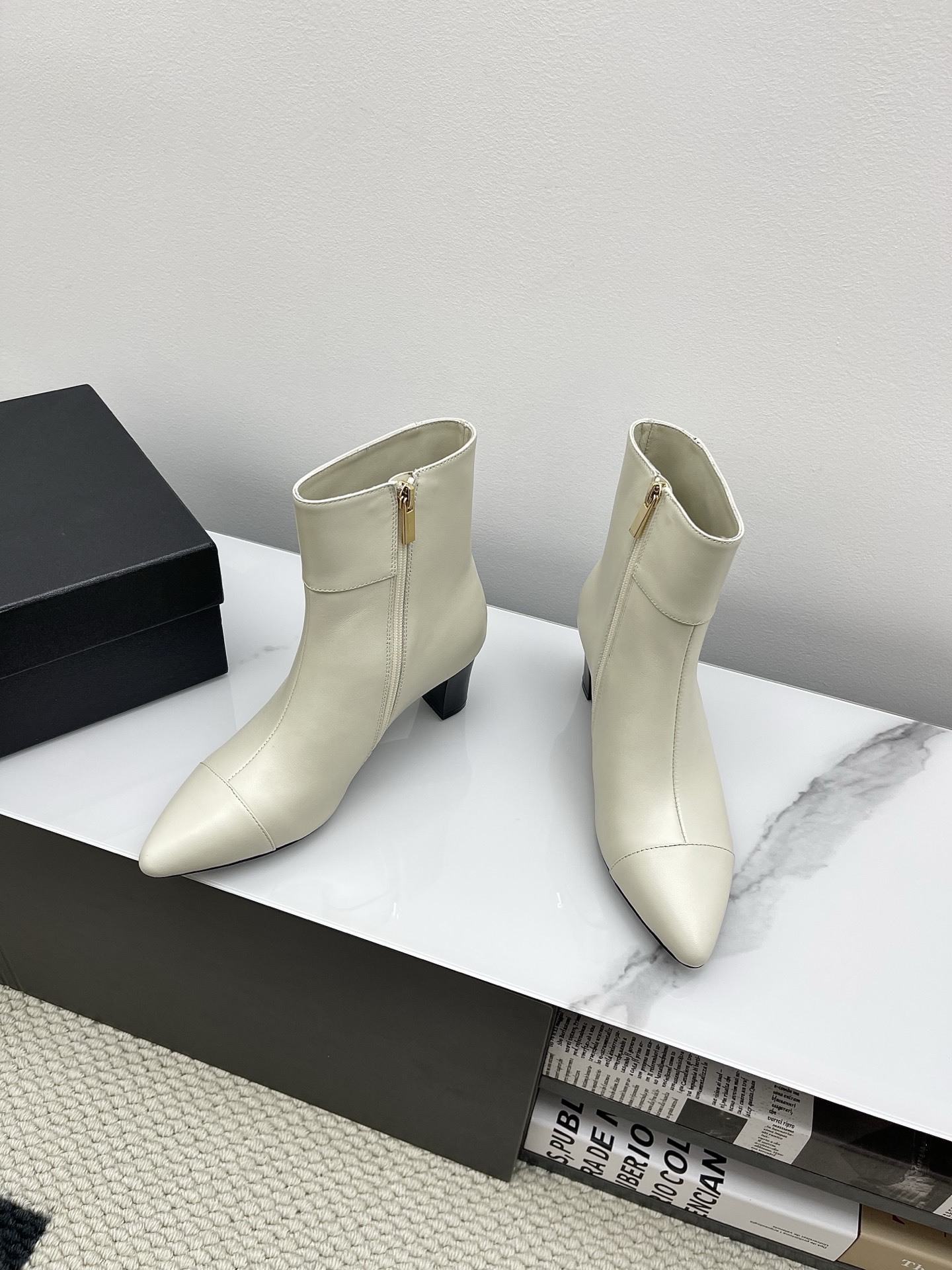 Pair of Chanel ivory leather pointed-toe ankle boots with gold lion head emblem and side zipper on a white marble surface. - Hình 8