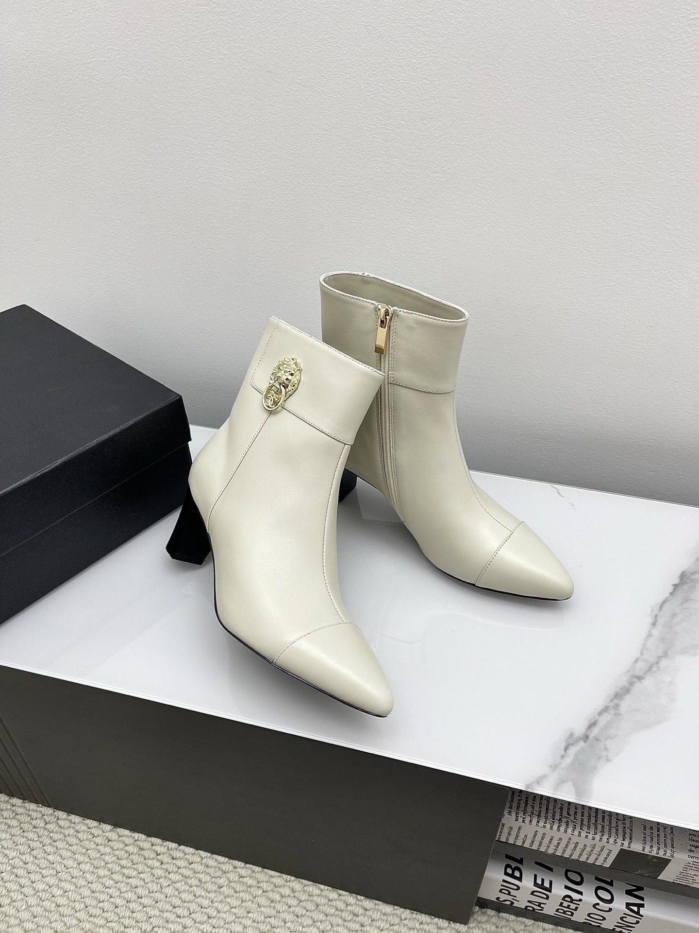 Pair of Chanel ivory leather pointed-toe ankle boots with gold lion head emblem and side zipper on a white marble surface. - Hình 3