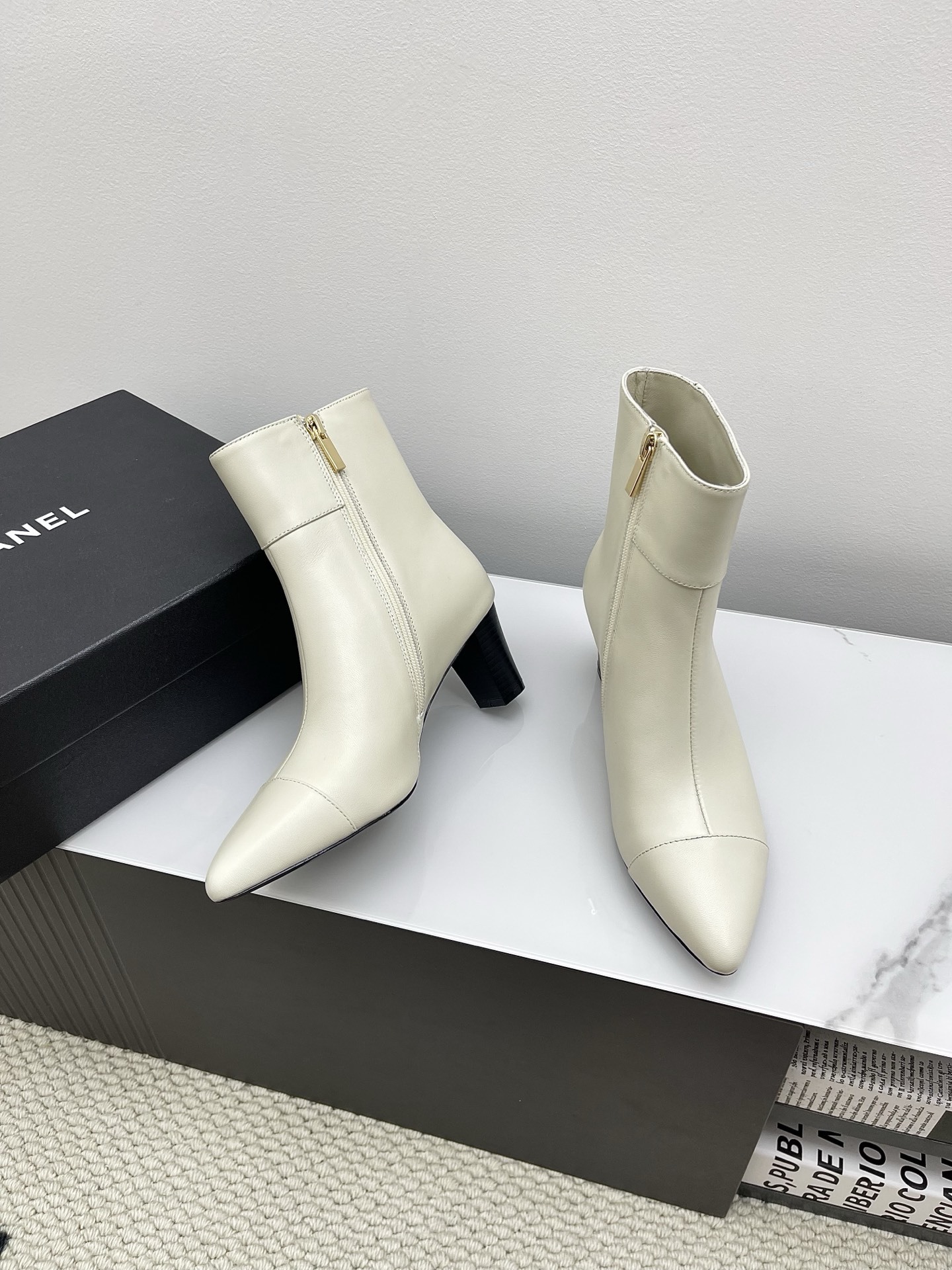 Pair of Chanel ivory leather pointed-toe ankle boots with gold lion head emblem and side zipper on a white marble surface. - Hình 2