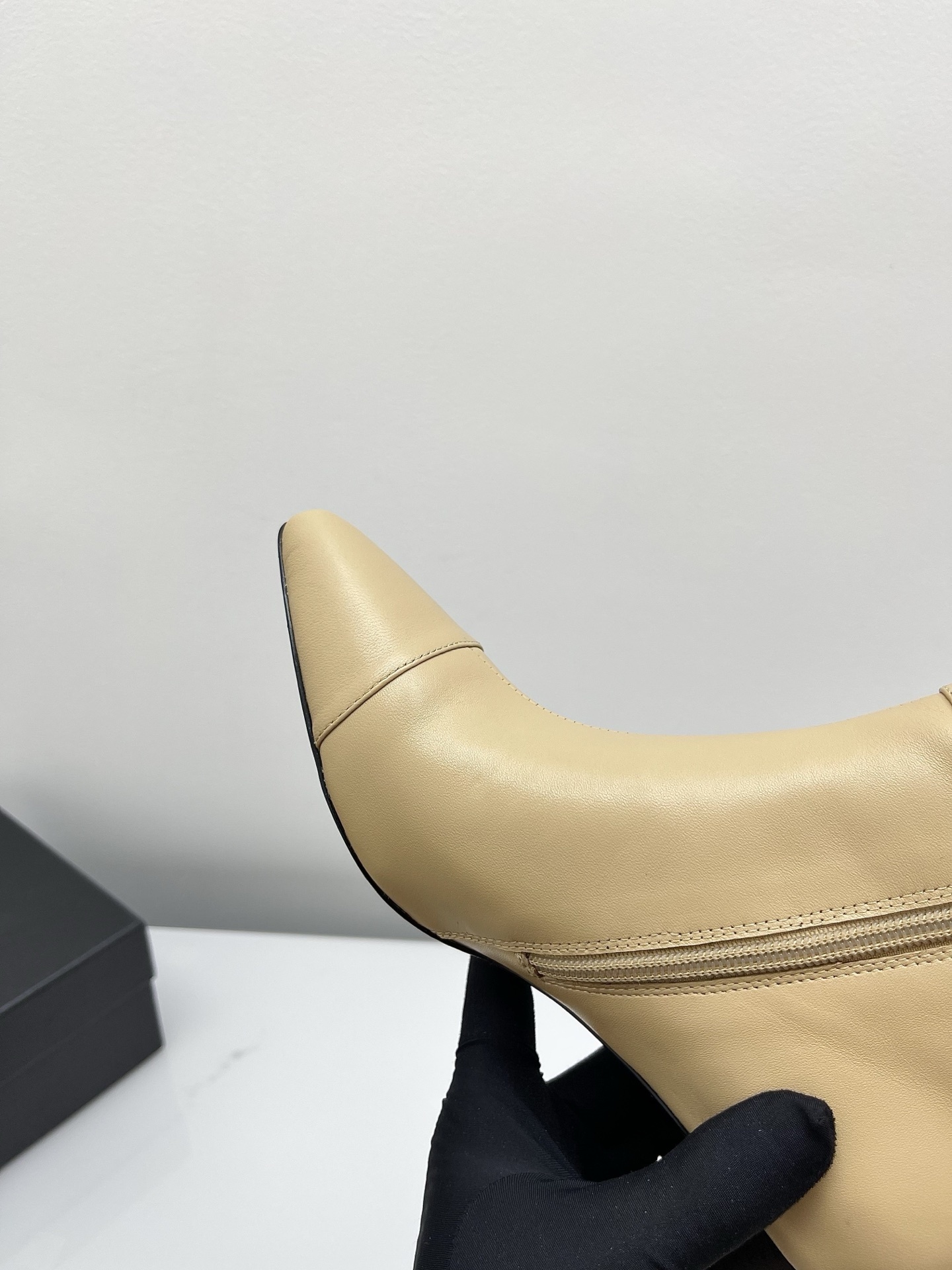 A pair of elegant beige leather pointed-toe ankle boots with a golden lion emblem and black block heel displayed on a white surface. - Hình 9