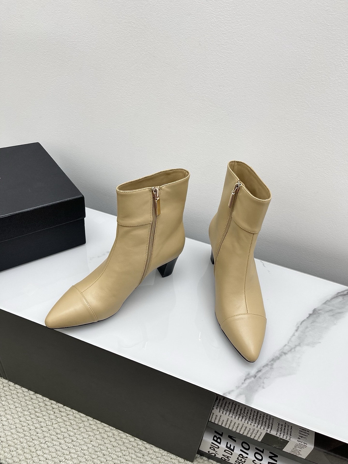 A pair of elegant beige leather pointed-toe ankle boots with a golden lion emblem and black block heel displayed on a white surface. - Hình 8