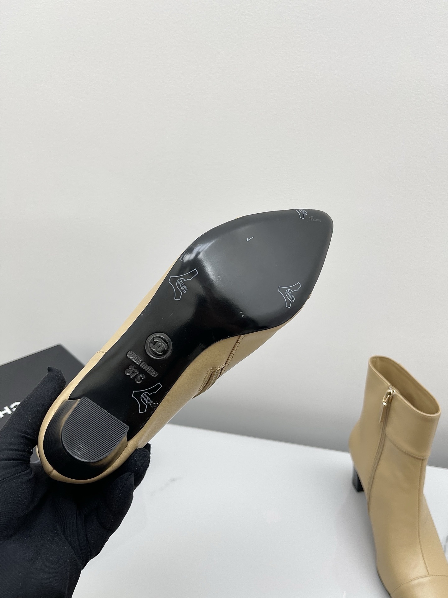 A pair of elegant beige leather pointed-toe ankle boots with a golden lion emblem and black block heel displayed on a white surface. - Hình 7