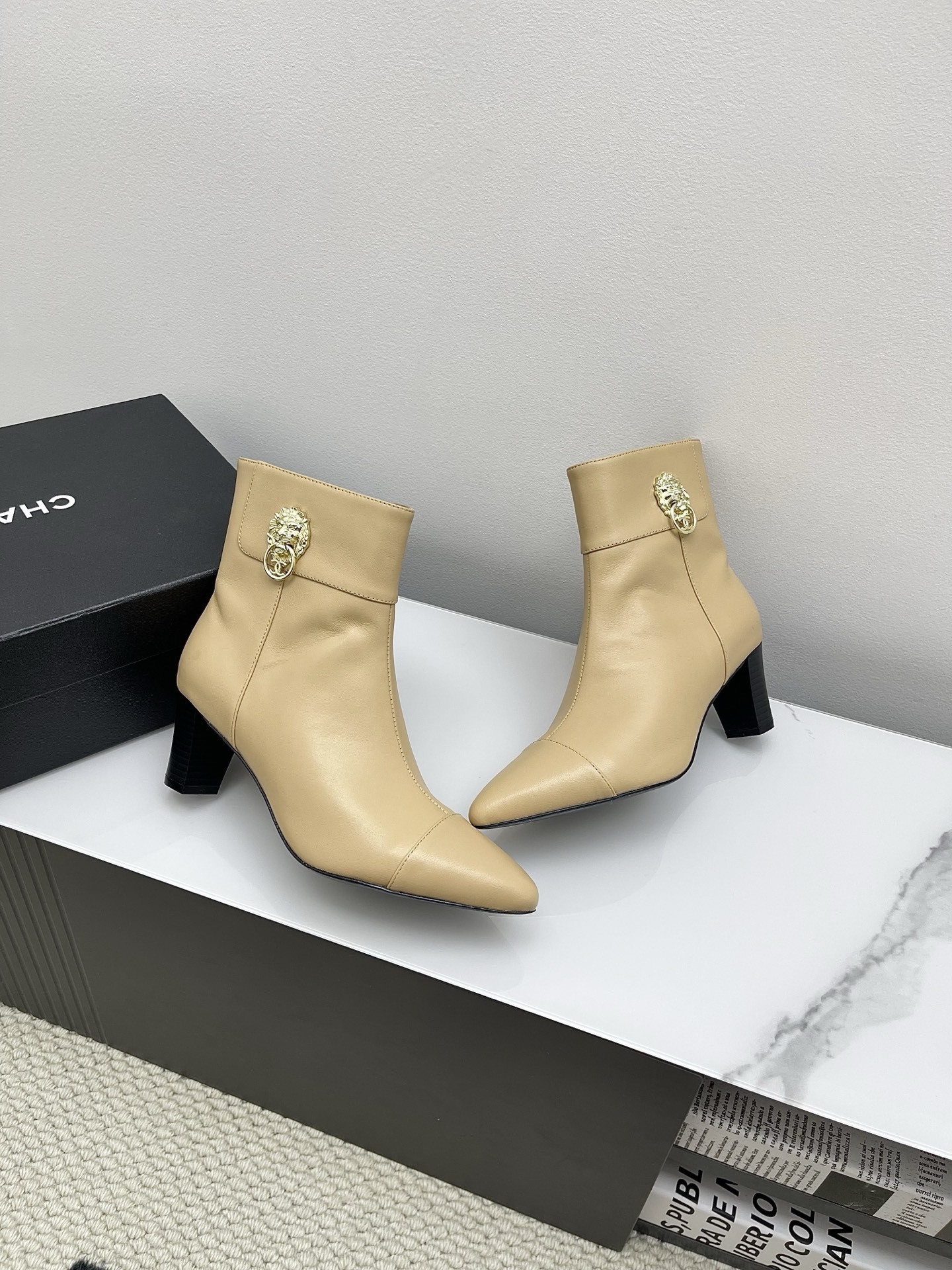 A pair of elegant beige leather pointed-toe ankle boots with a golden lion emblem and black block heel displayed on a white surface. - Hình 6