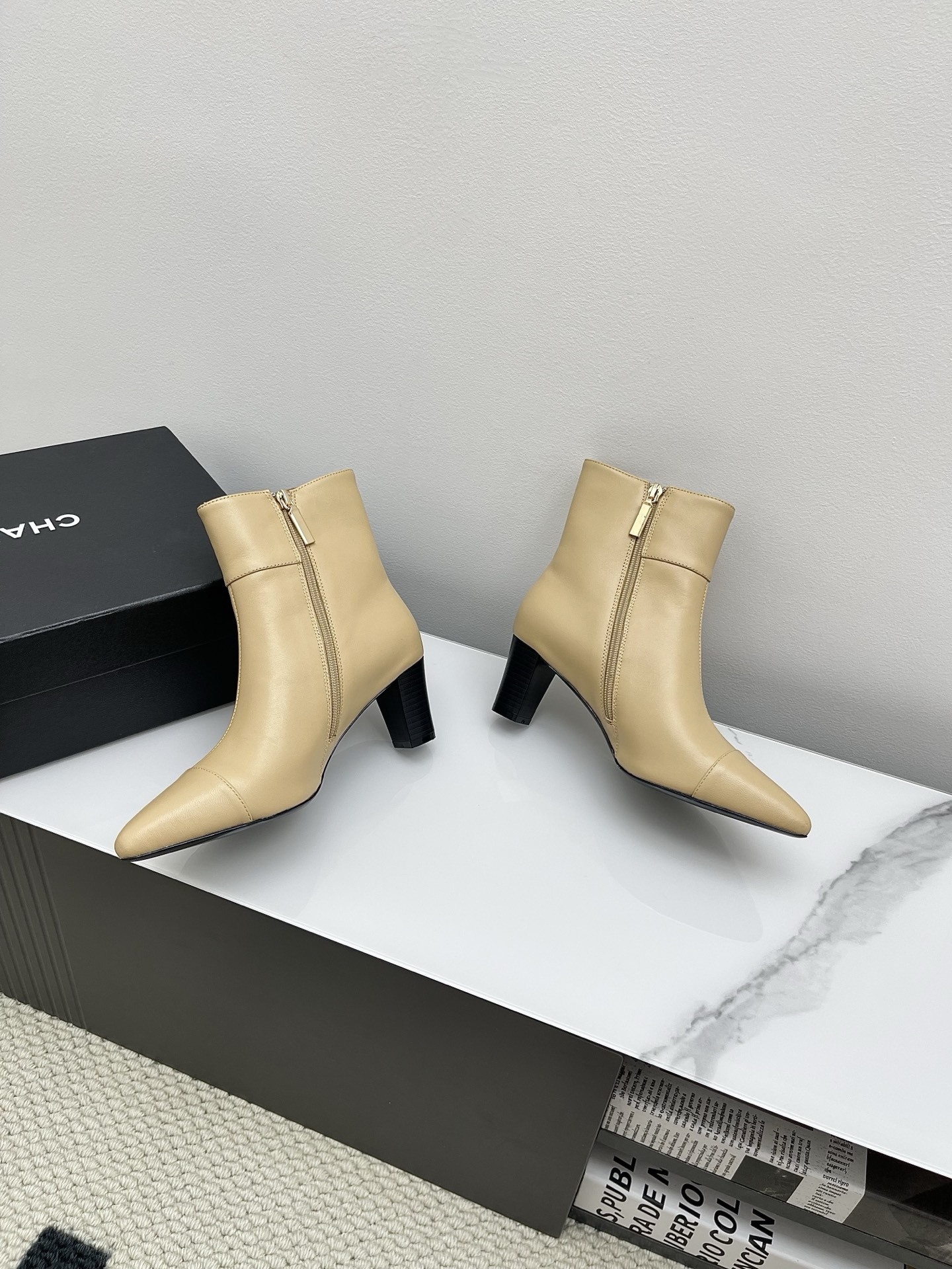 A pair of elegant beige leather pointed-toe ankle boots with a golden lion emblem and black block heel displayed on a white surface. - Hình 5
