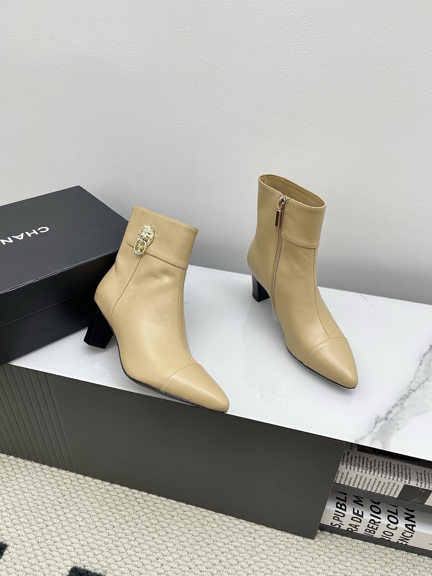 A pair of elegant beige leather pointed-toe ankle boots with a golden lion emblem and black block heel displayed on a white surface. - Hình 4