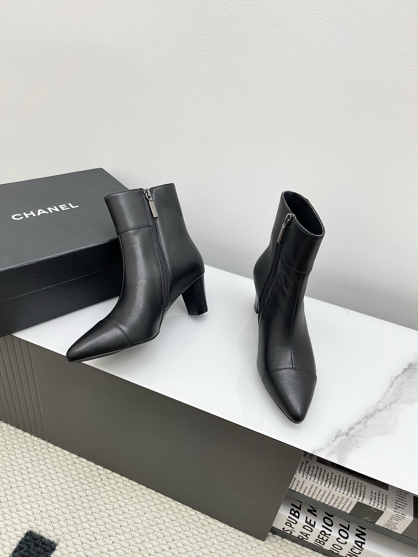 Chanel black leather pointed-toe ankle boots with side zippers and block heels shown next to a signature Chanel box. - Hình 2