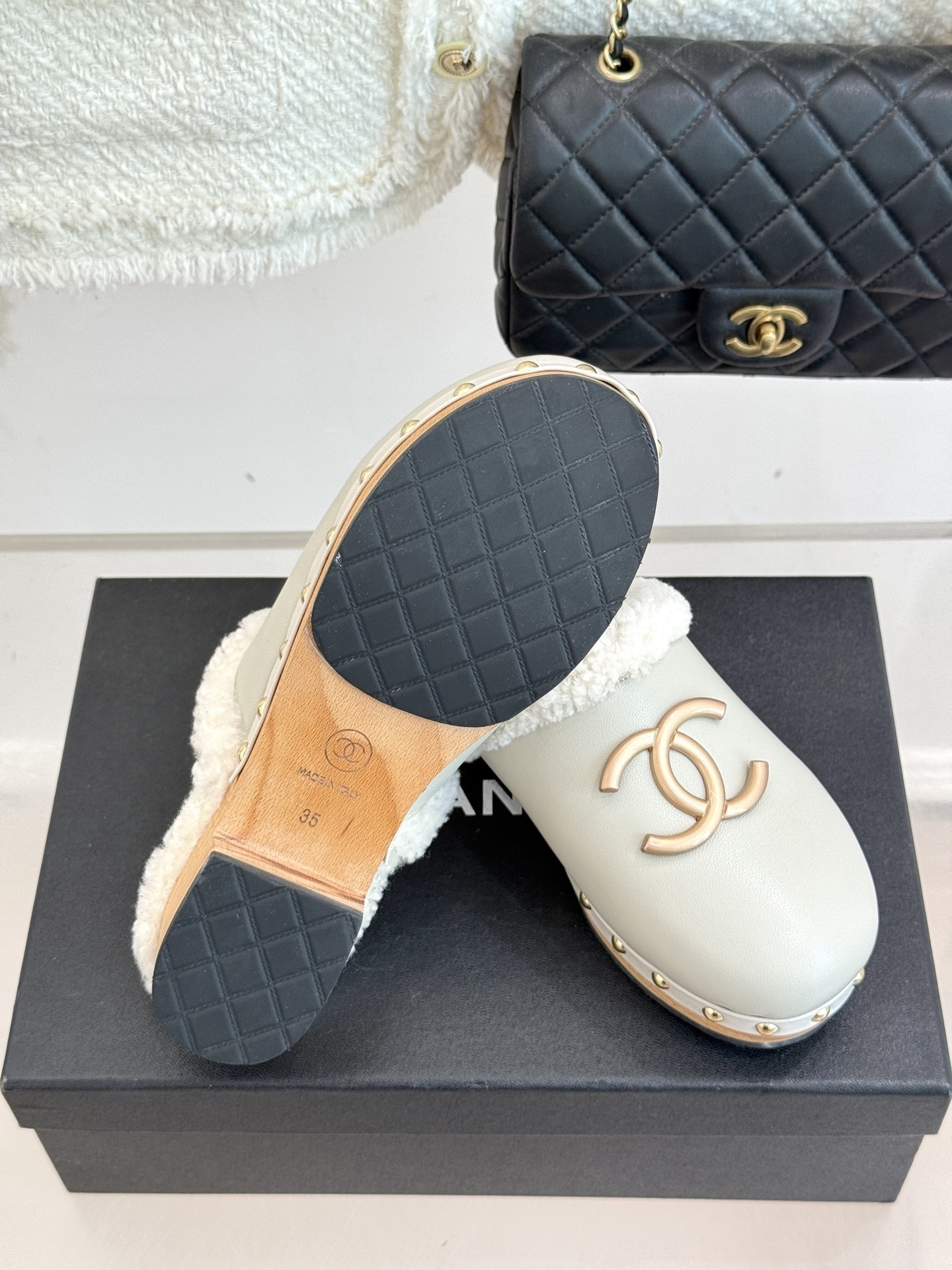 Pair of luxury off-white Chanel leather clogs with shearling lining and gold-tone CC logo displayed on a black box. - Hình 9