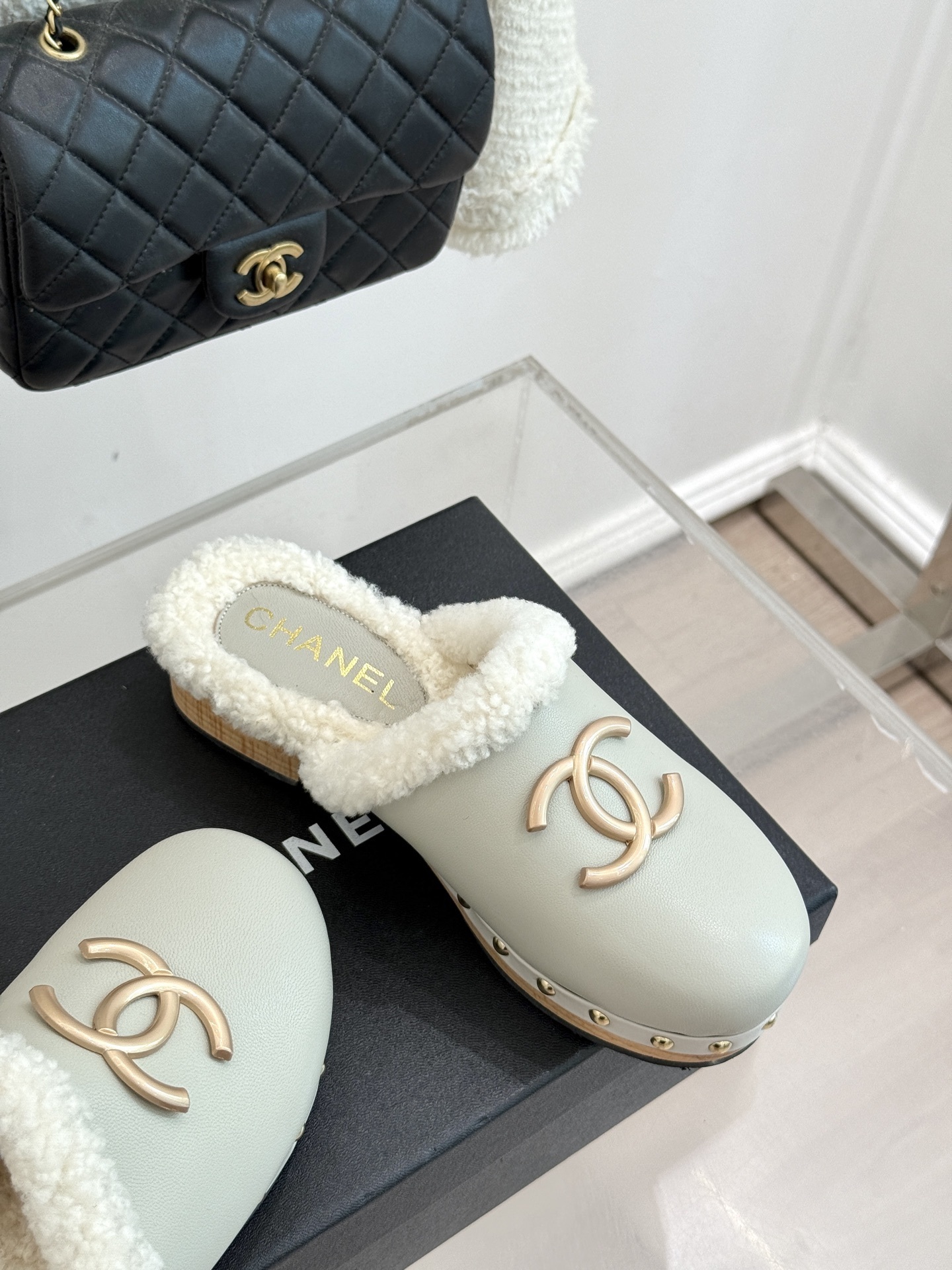 Pair of luxury off-white Chanel leather clogs with shearling lining and gold-tone CC logo displayed on a black box. - Hình 5