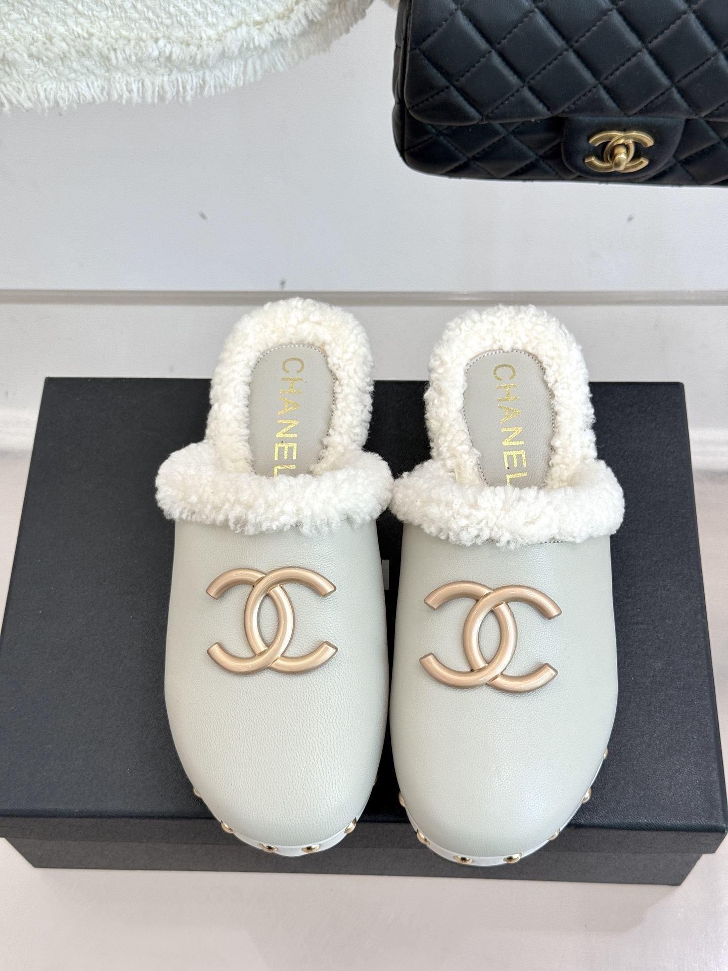 Pair of luxury off-white Chanel leather clogs with shearling lining and gold-tone CC logo displayed on a black box. - Hình 4