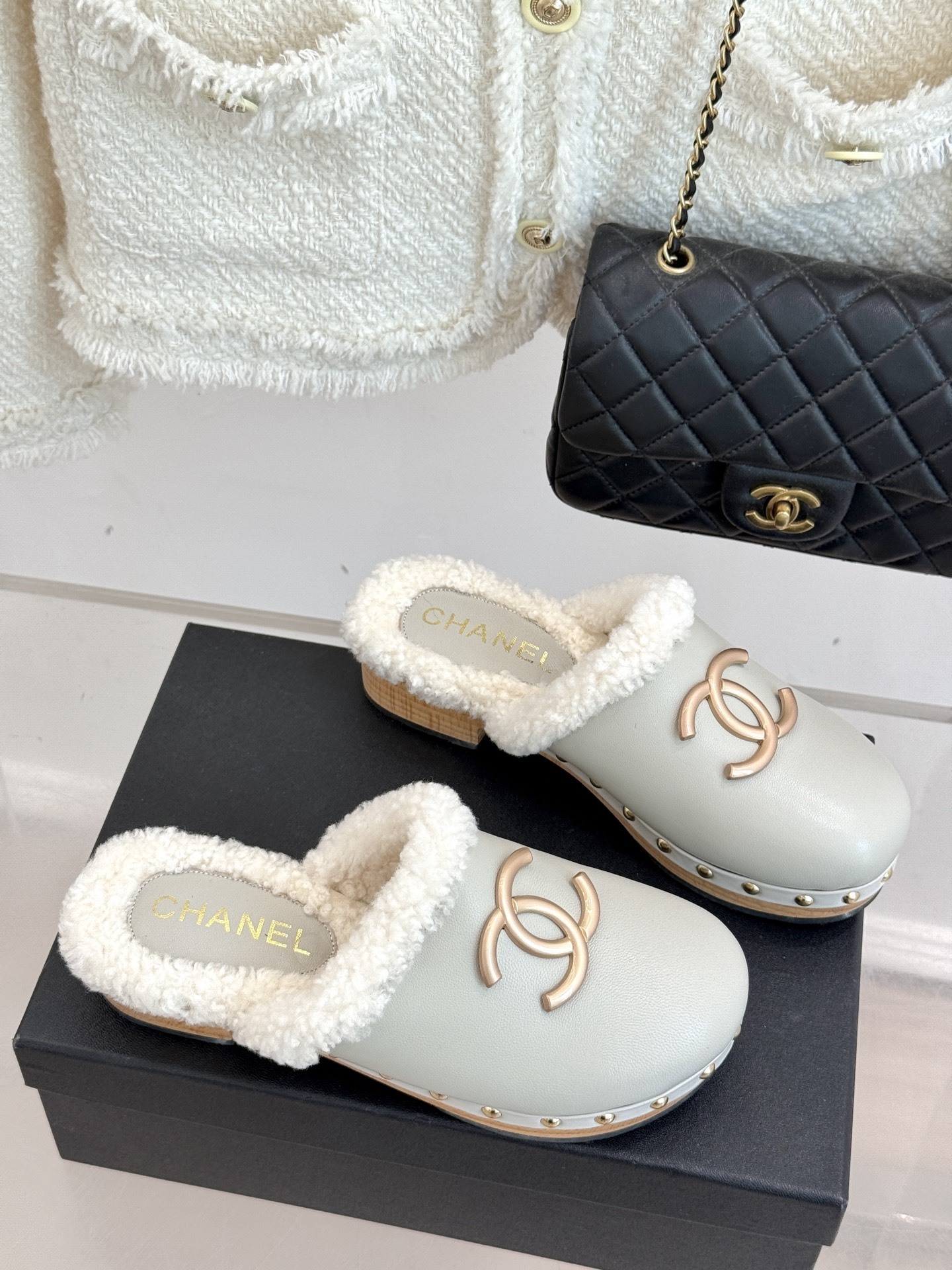 Pair of luxury off-white Chanel leather clogs with shearling lining and gold-tone CC logo displayed on a black box. - Hình 3