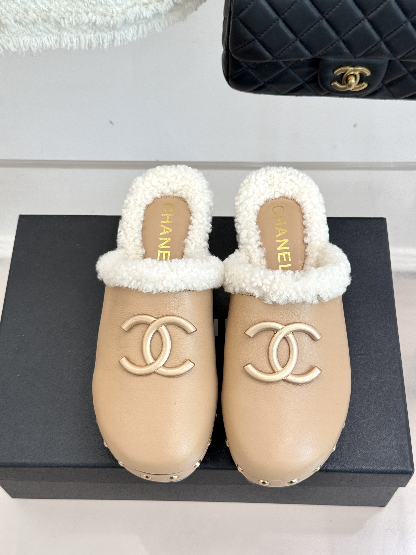 Pair of luxury Chanel beige leather clogs with white shearling lining and gold CC logo displayed on a black box - Hình 4