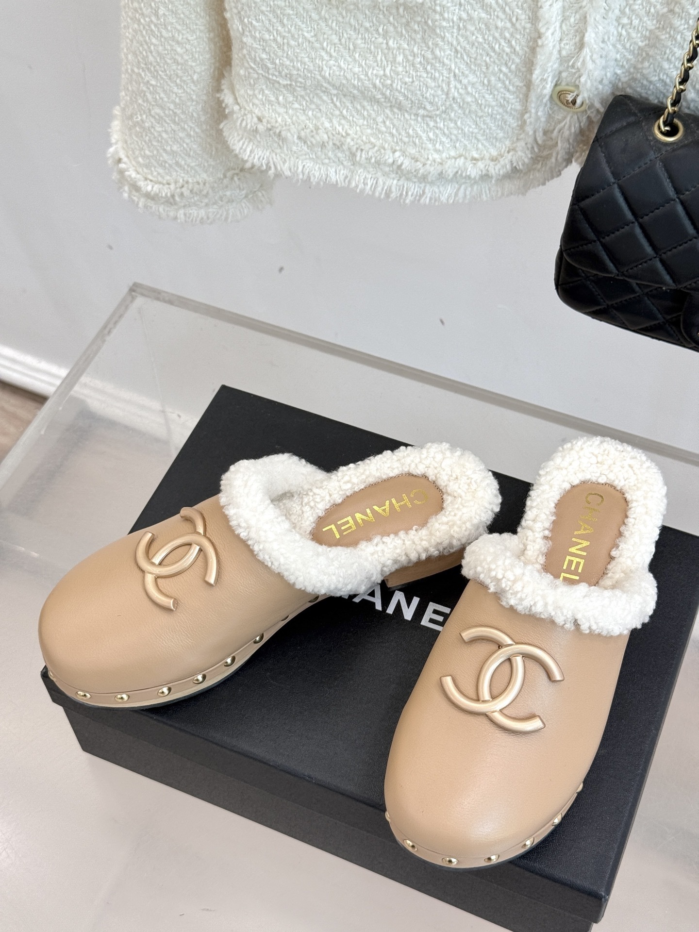 Pair of luxury Chanel beige leather clogs with white shearling lining and gold CC logo displayed on a black box - Hình 2