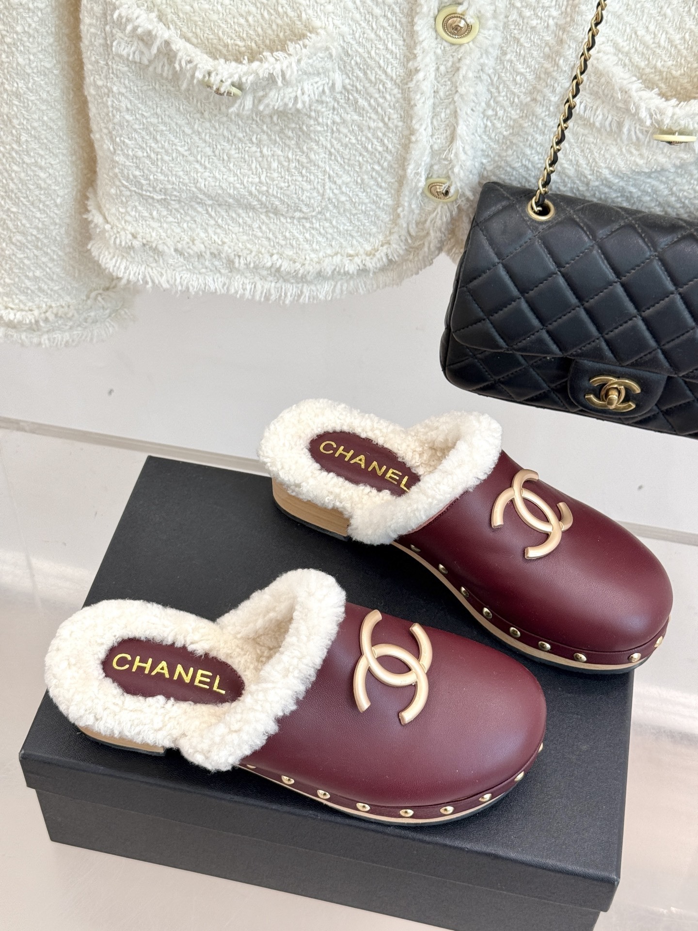 Pair of burgundy Chanel leather clogs with white shearling lining and gold CC logo on a black box - Hình 3