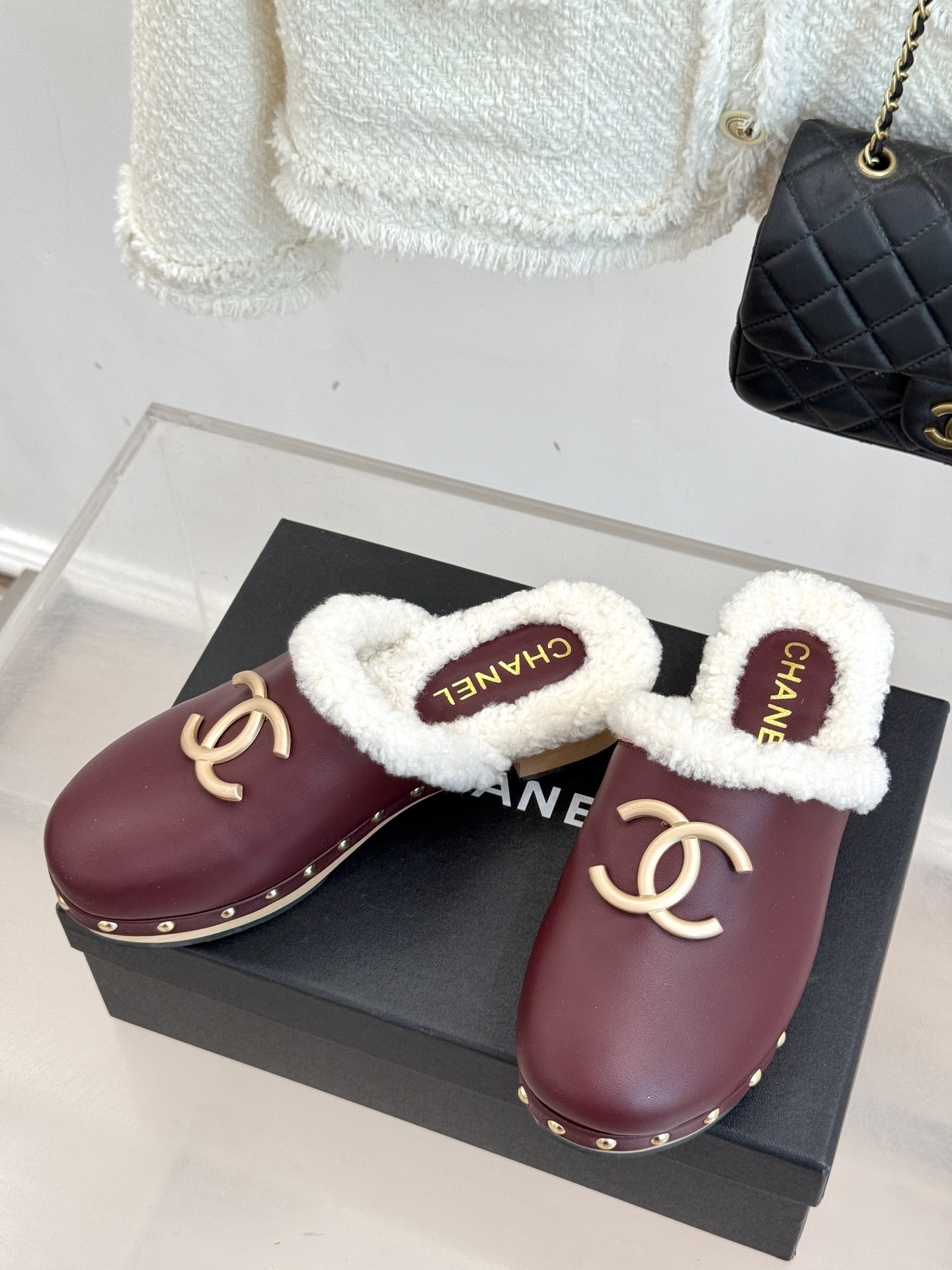 Pair of burgundy Chanel leather clogs with white shearling lining and gold CC logo on a black box - Hình 2