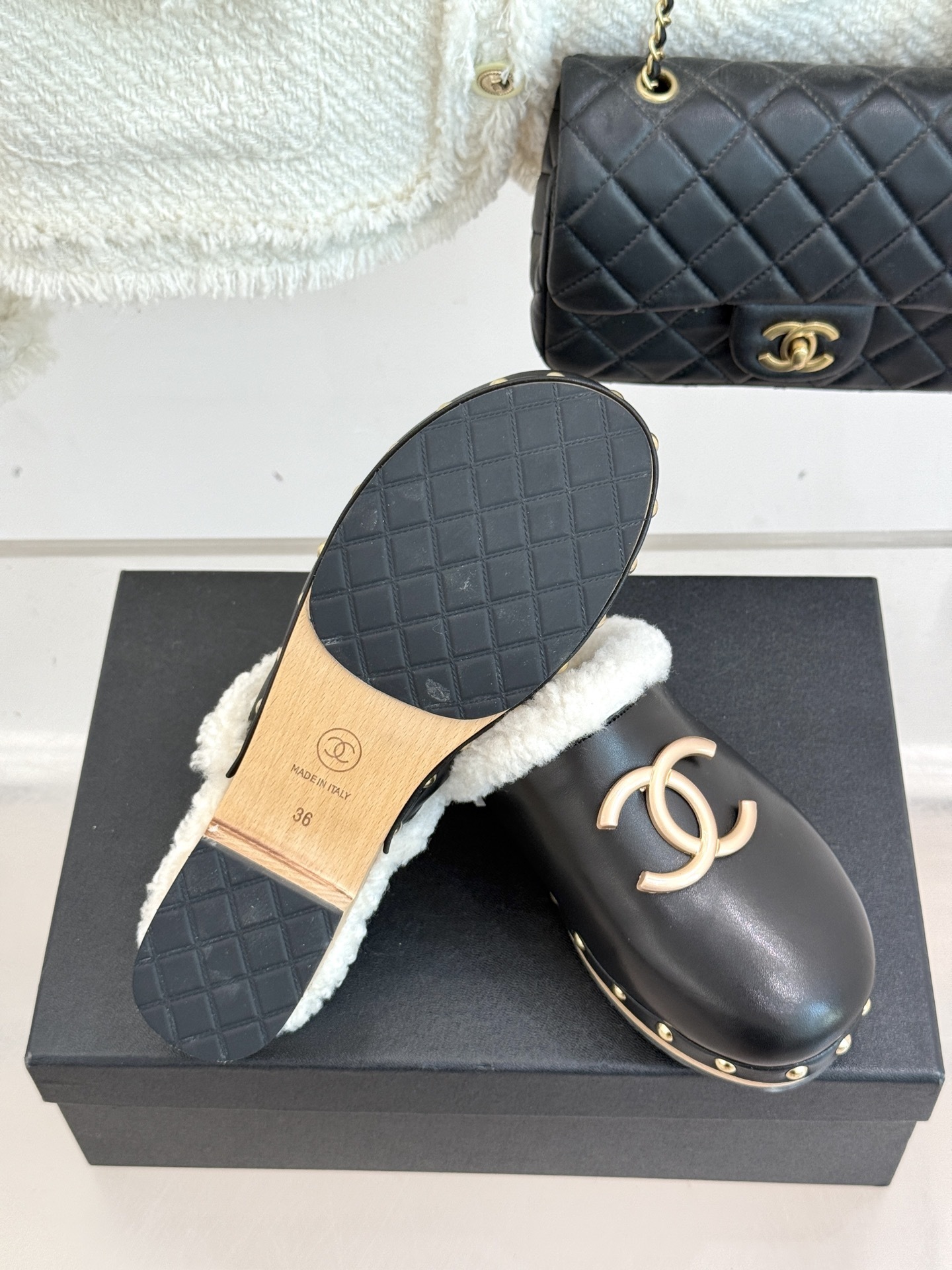 Pair of Chanel black leather clogs with white shearling lining, gold CC logo, and studded wooden soles resting on a black box - Hình 9