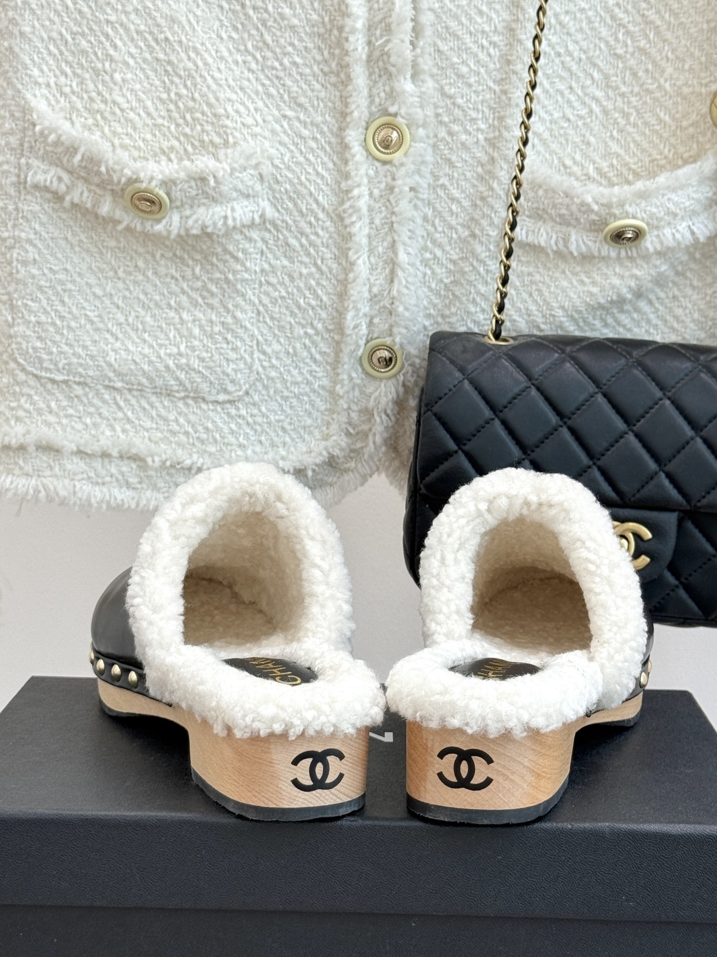 Pair of Chanel black leather clogs with white shearling lining, gold CC logo, and studded wooden soles resting on a black box - Hình 6