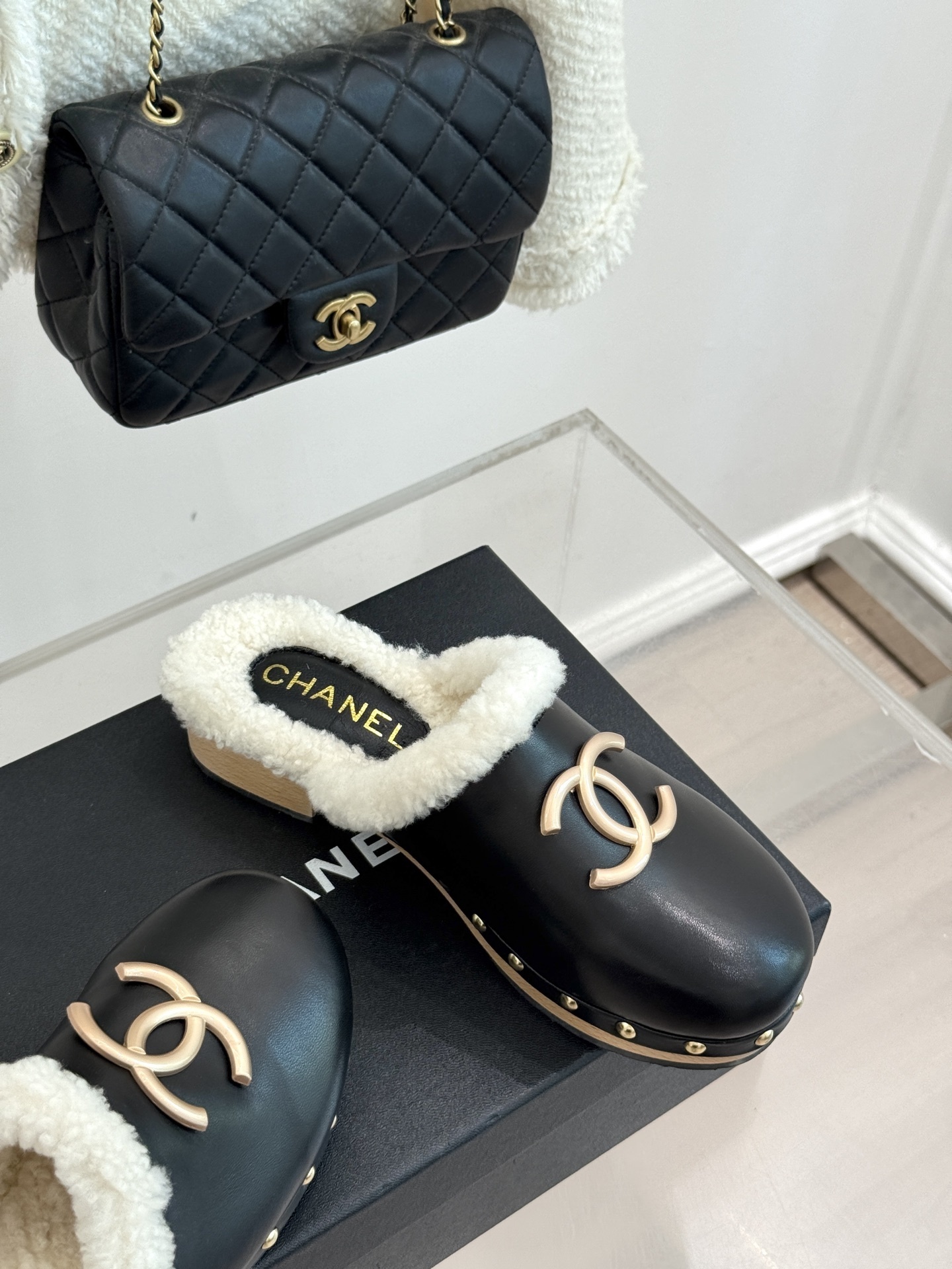 Pair of Chanel black leather clogs with white shearling lining, gold CC logo, and studded wooden soles resting on a black box - Hình 5