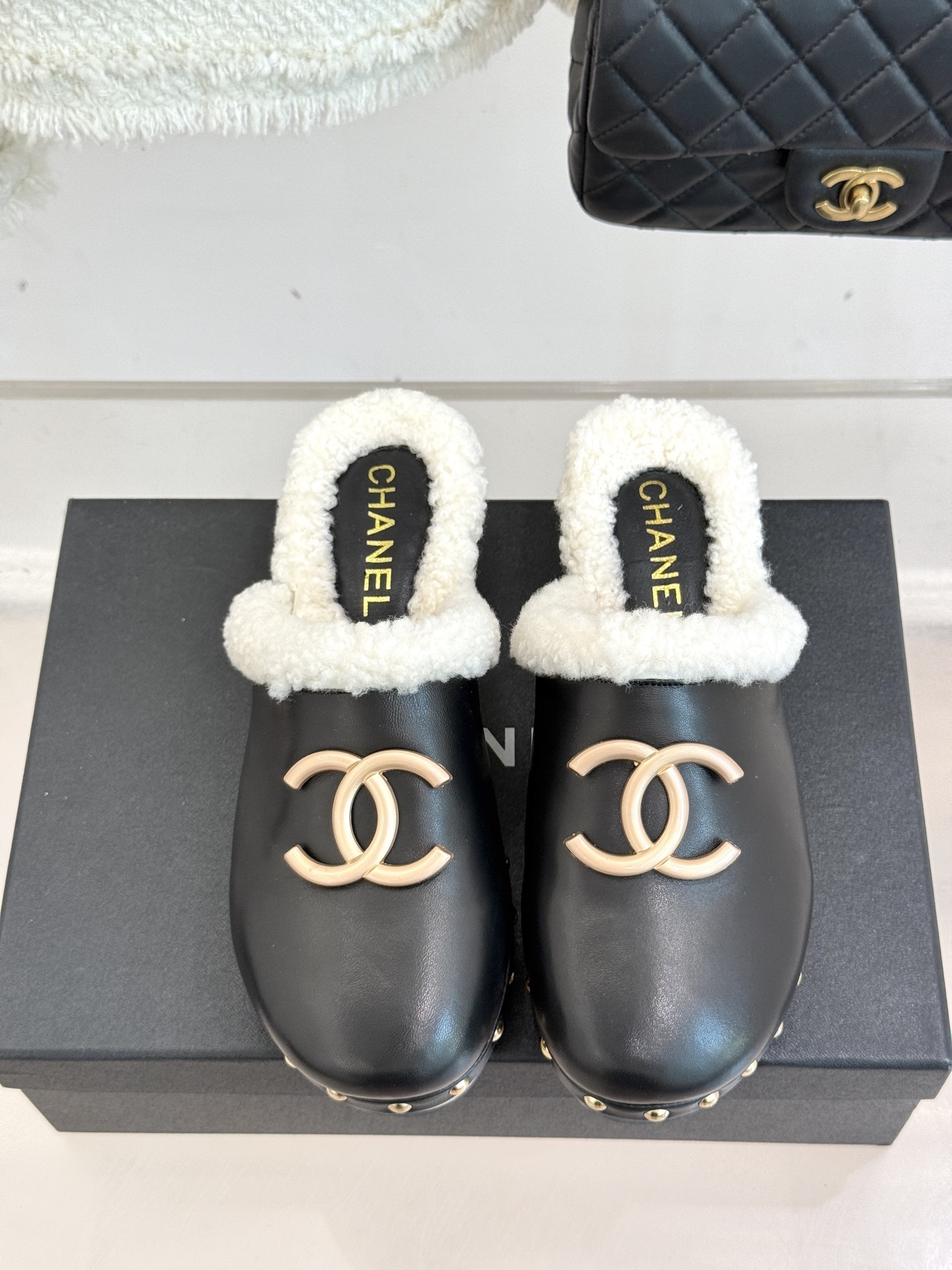 Pair of Chanel black leather clogs with white shearling lining, gold CC logo, and studded wooden soles resting on a black box - Hình 4