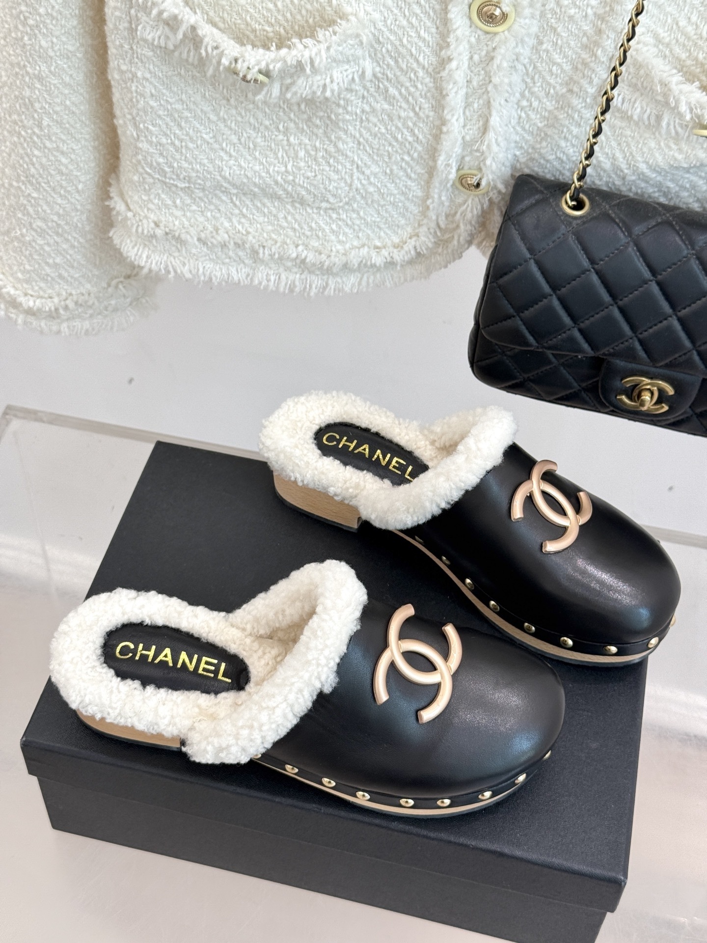 Pair of Chanel black leather clogs with white shearling lining, gold CC logo, and studded wooden soles resting on a black box - Hình 3