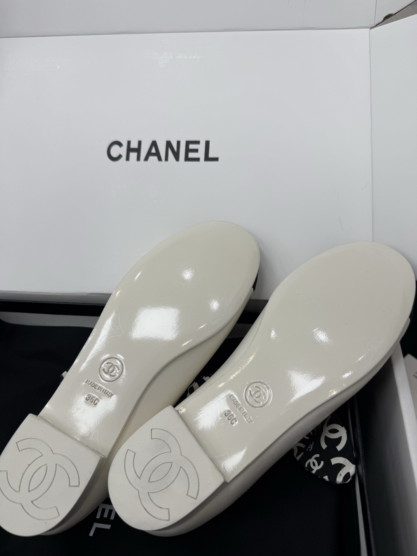 A pair of Chanel white leather ballet flats with black toe caps and a decorative black and white CC logo ribbon bow, presented in a Chanel box. - Hình 9