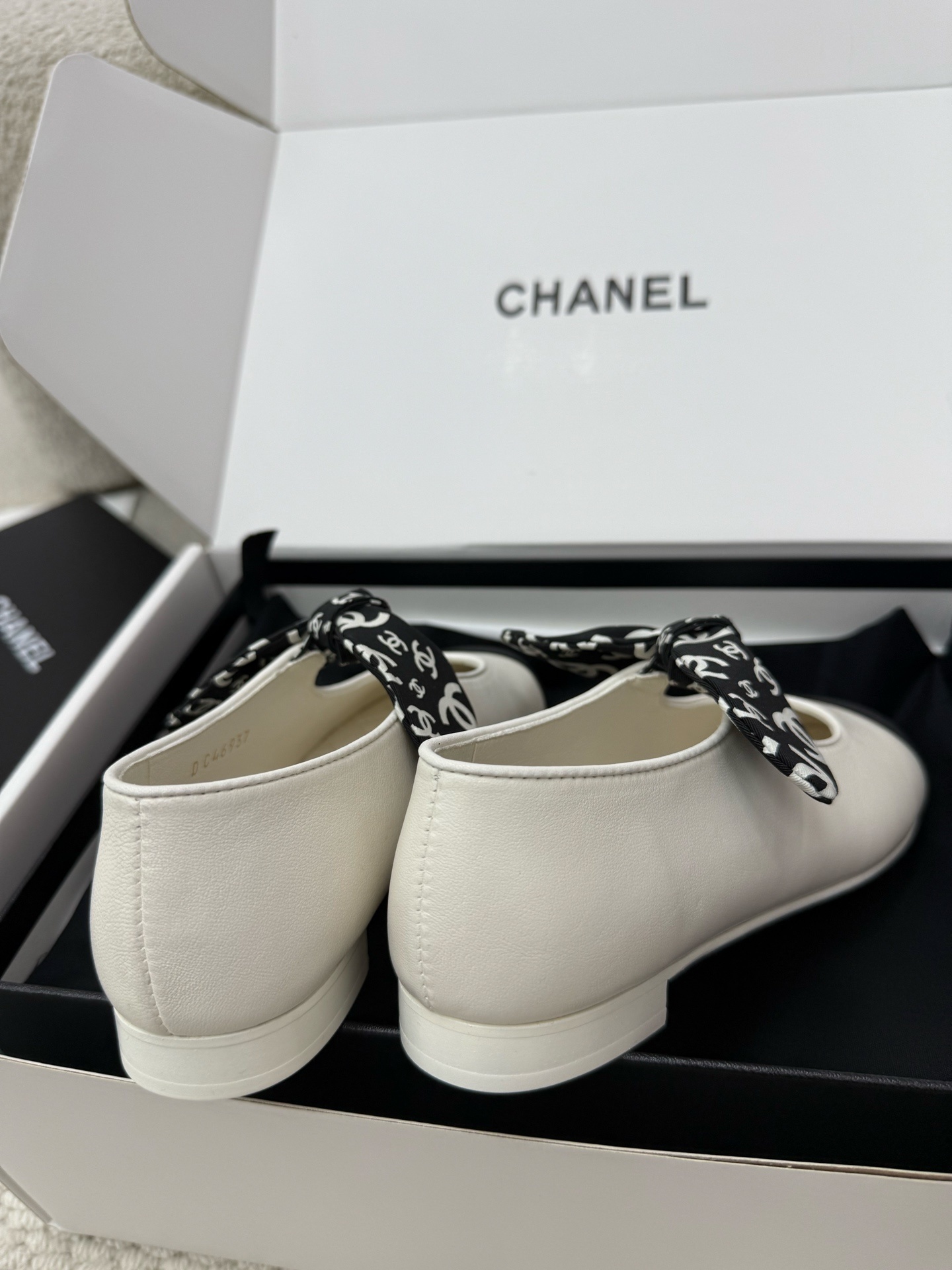 A pair of Chanel white leather ballet flats with black toe caps and a decorative black and white CC logo ribbon bow, presented in a Chanel box. - Hình 8