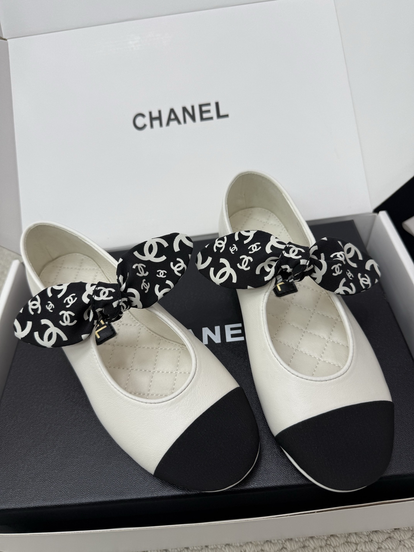 A pair of Chanel white leather ballet flats with black toe caps and a decorative black and white CC logo ribbon bow, presented in a Chanel box. - Hình 5