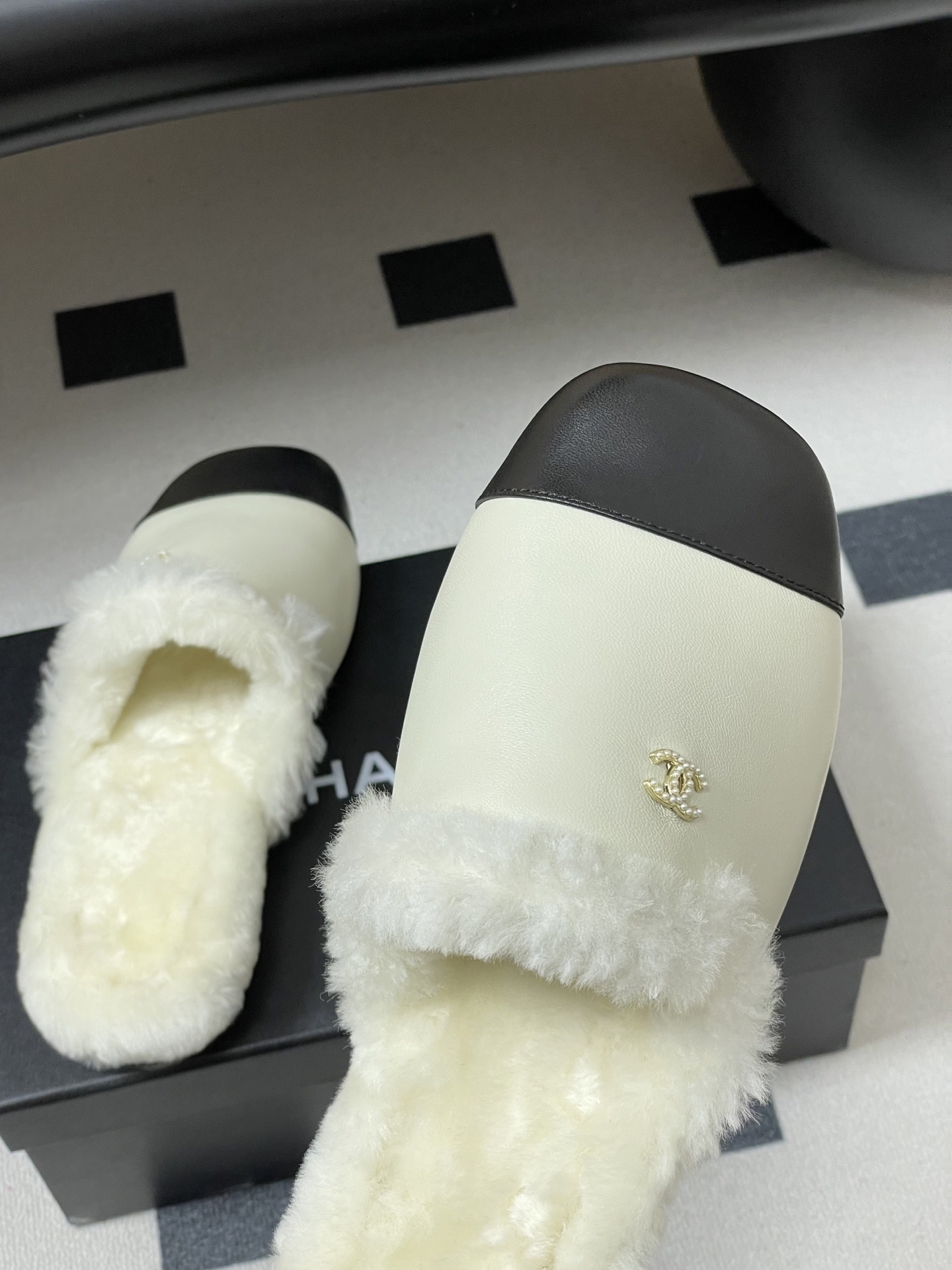 Luxury cream leather mules with black cap toe and white faux fur lining shown on a black surface. - Hình 9