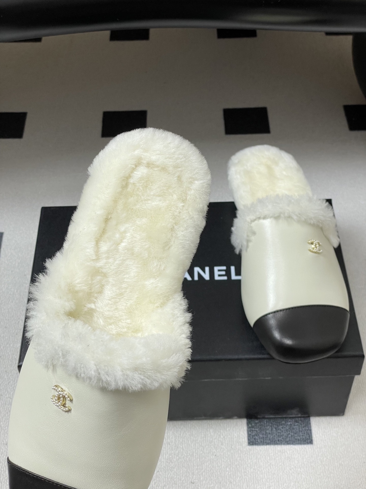 Luxury cream leather mules with black cap toe and white faux fur lining shown on a black surface. - Hình 7