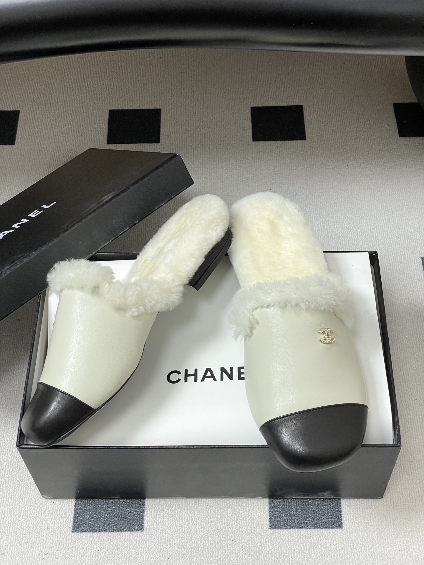 Luxury cream leather mules with black cap toe and white faux fur lining shown on a black surface. - Hình 6