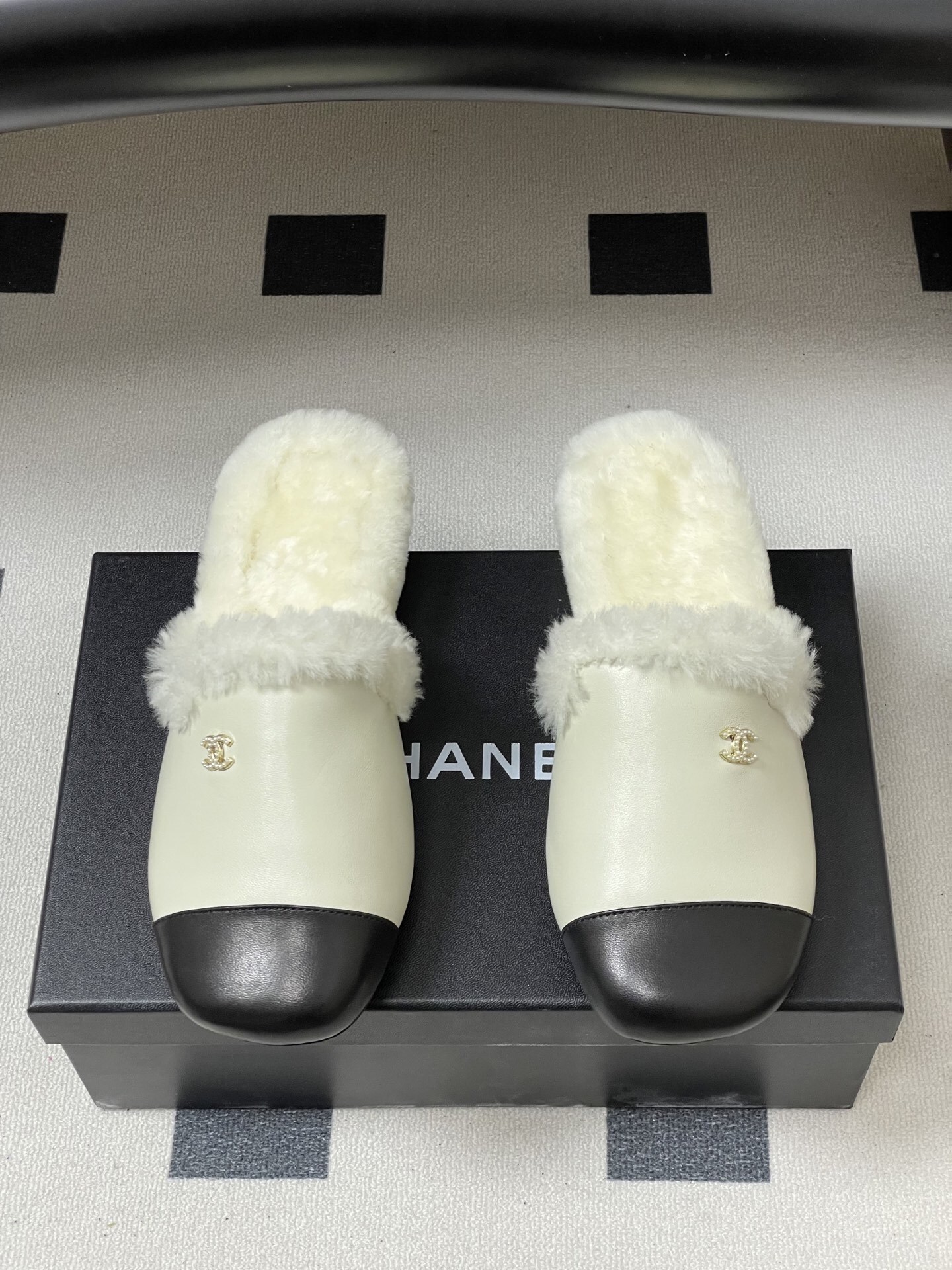 Luxury cream leather mules with black cap toe and white faux fur lining shown on a black surface. - Hình 5