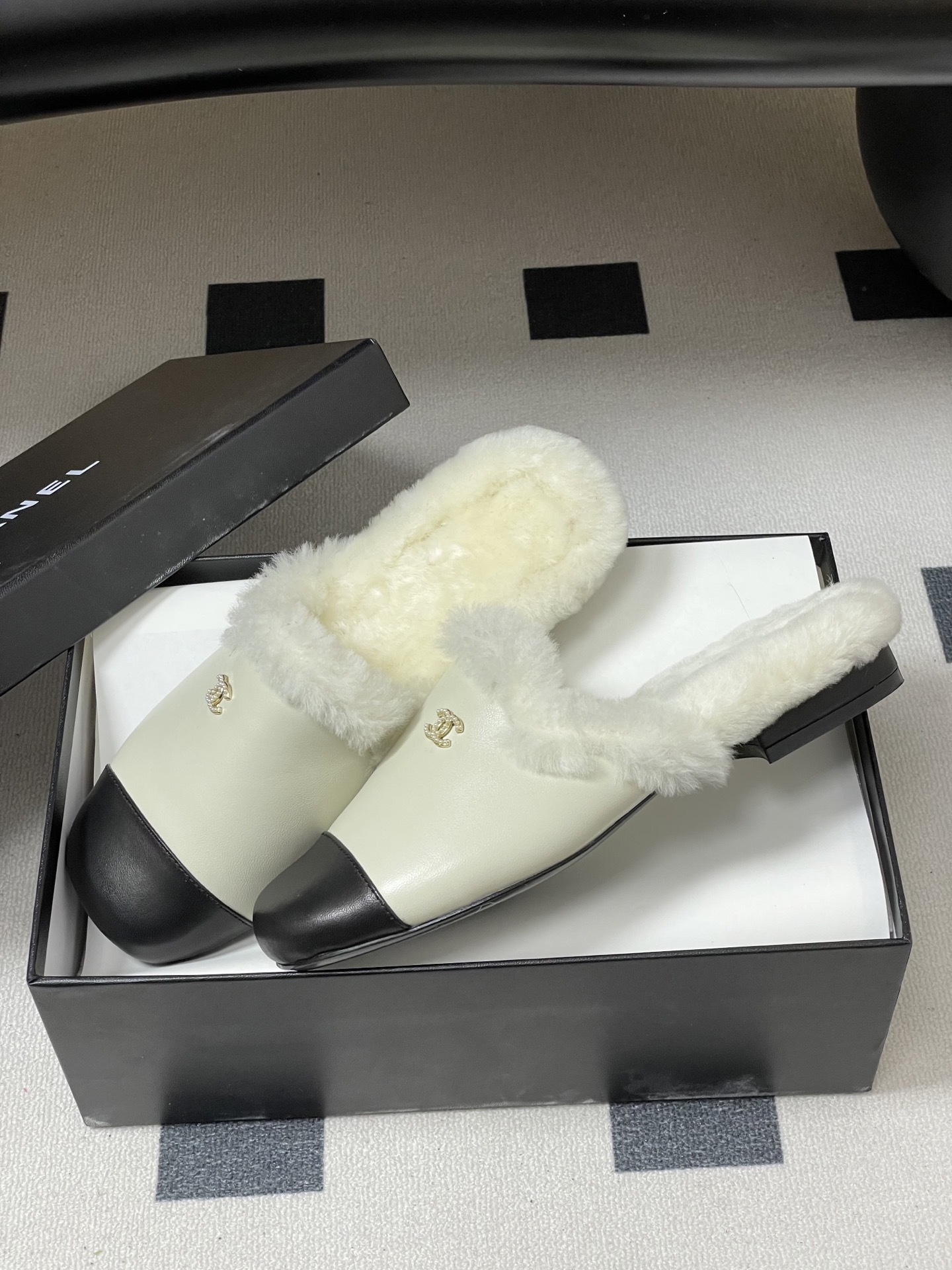 Luxury cream leather mules with black cap toe and white faux fur lining shown on a black surface. - Hình 4