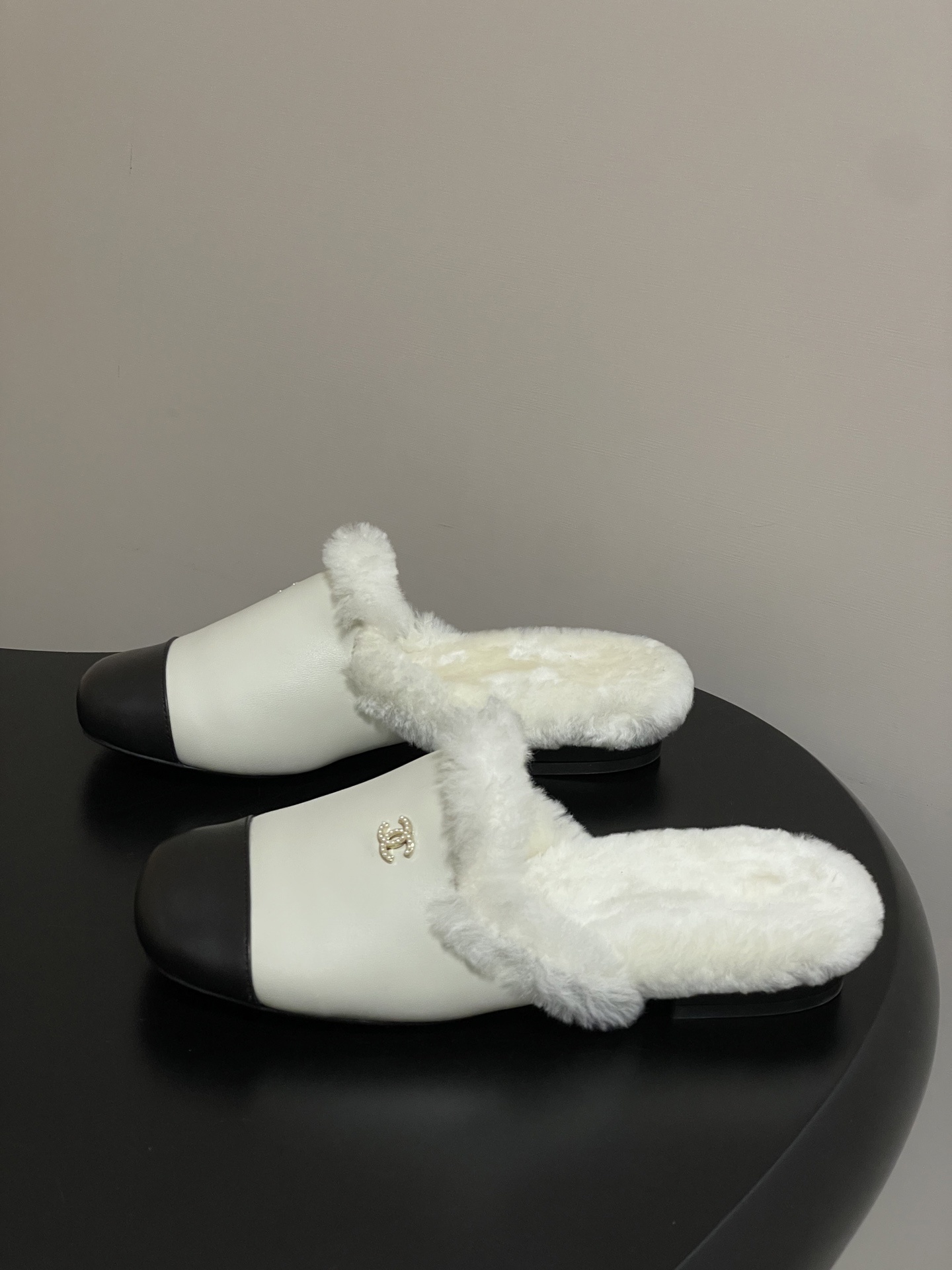 Luxury cream leather mules with black cap toe and white faux fur lining shown on a black surface. - Hình 3