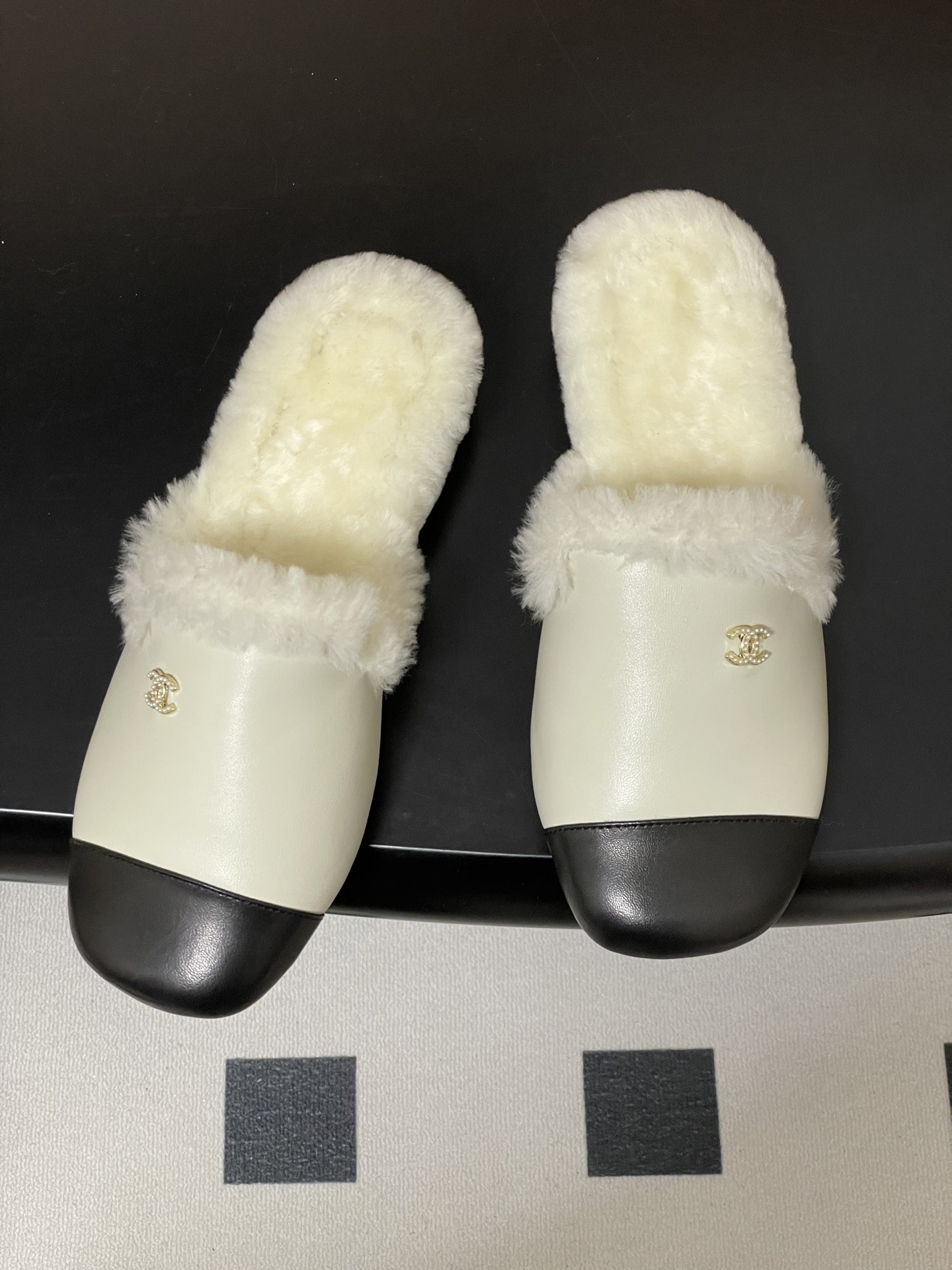 Luxury cream leather mules with black cap toe and white faux fur lining shown on a black surface. - Hình 2