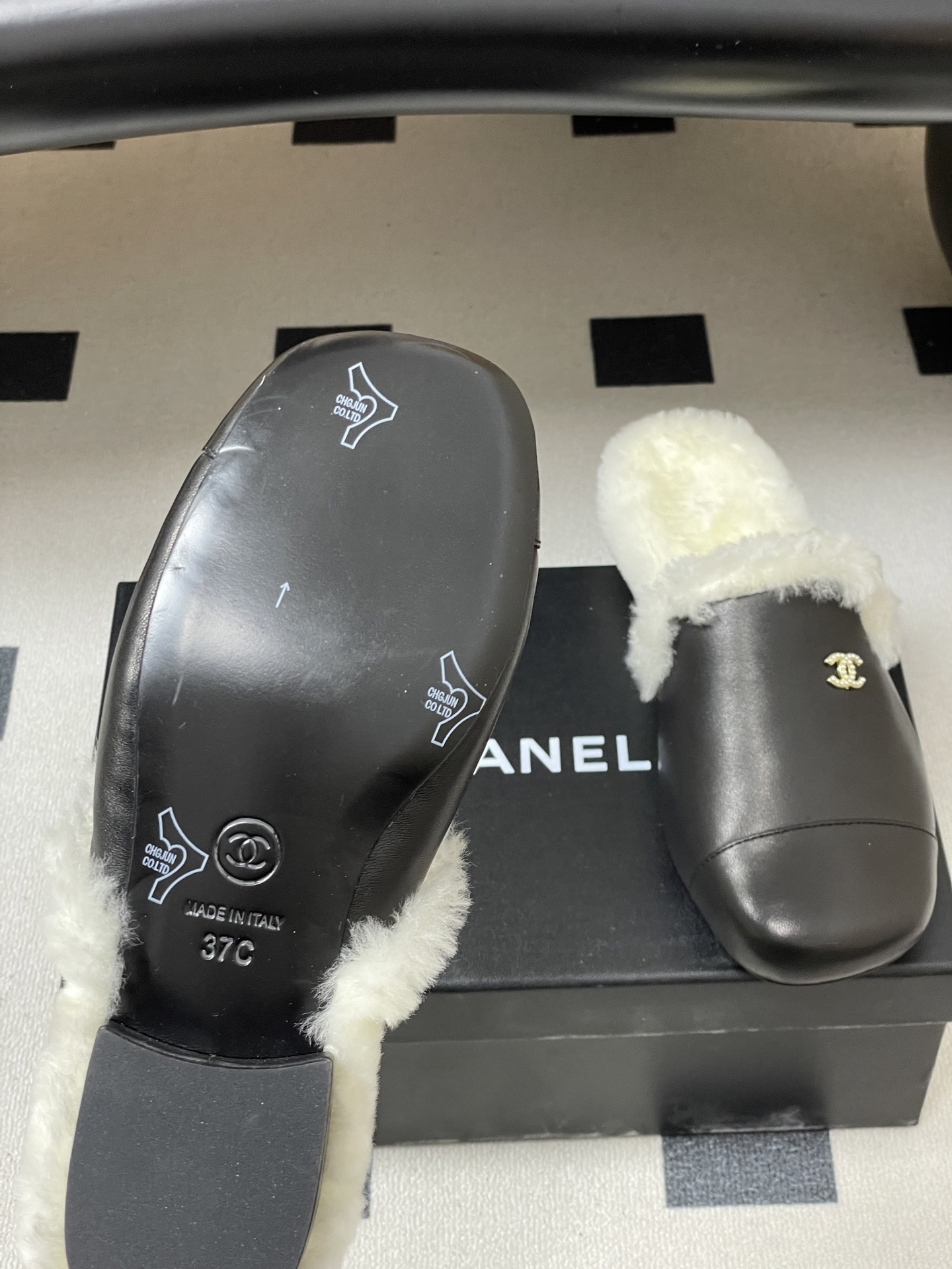 Pair of black leather mules with white shearling lining and gold interlocking logo on a black surface - Hình 8