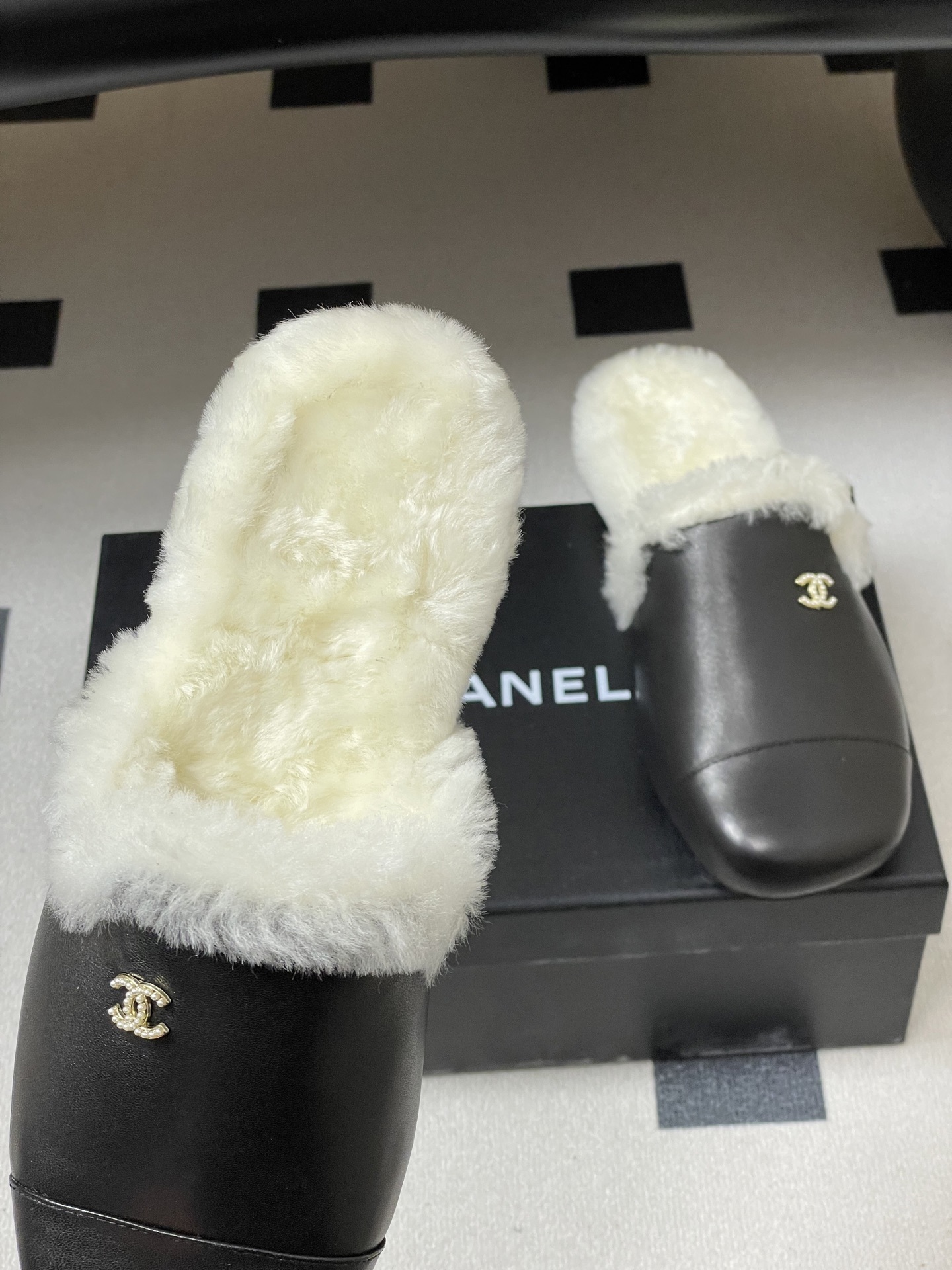 Pair of black leather mules with white shearling lining and gold interlocking logo on a black surface - Hình 7