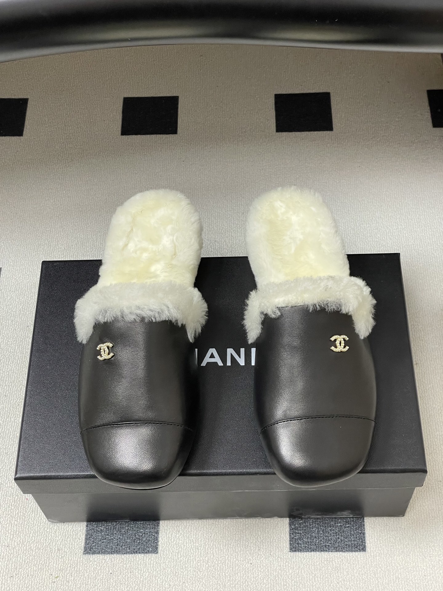 Pair of black leather mules with white shearling lining and gold interlocking logo on a black surface - Hình 5