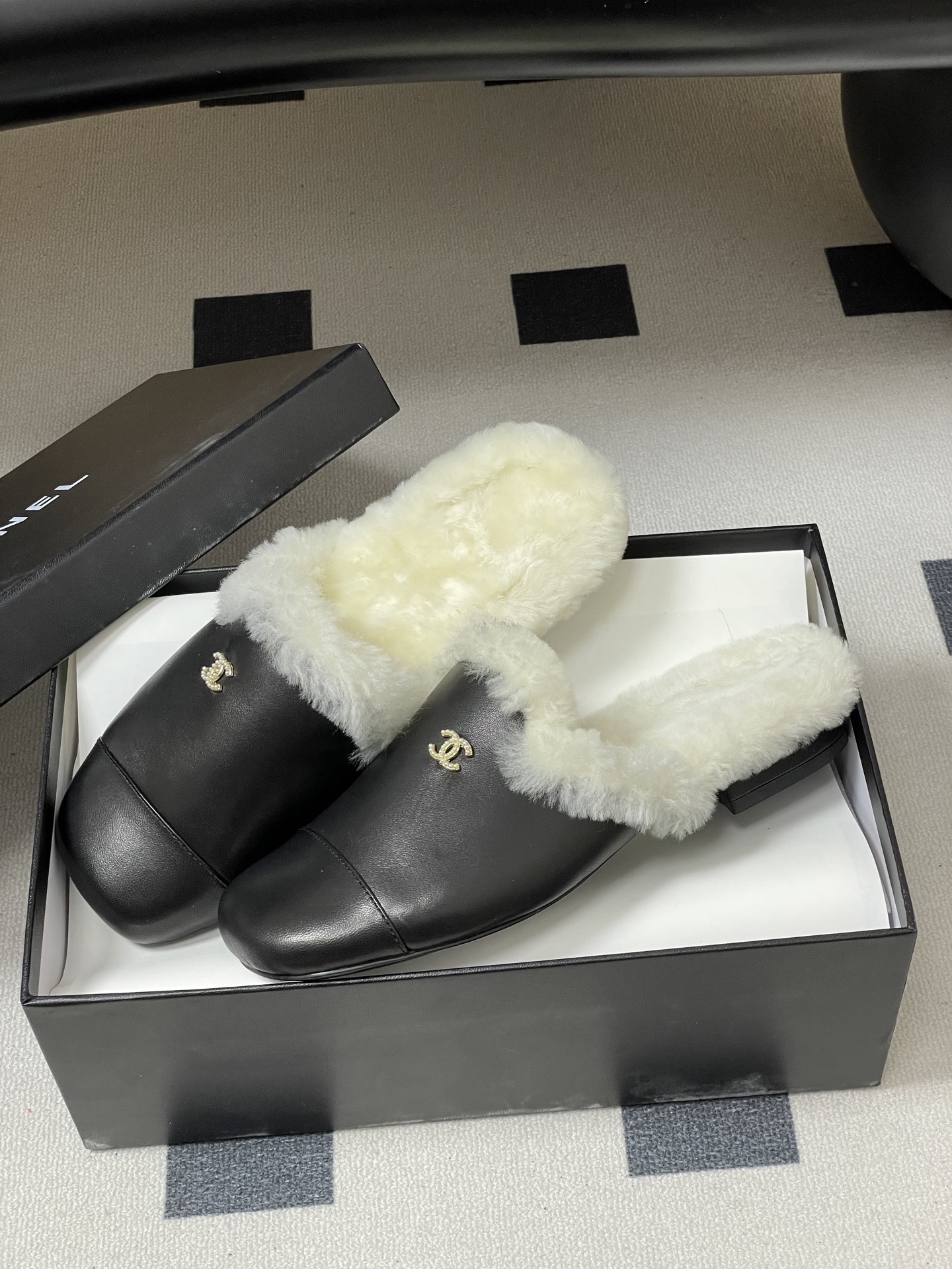 Pair of black leather mules with white shearling lining and gold interlocking logo on a black surface - Hình 4