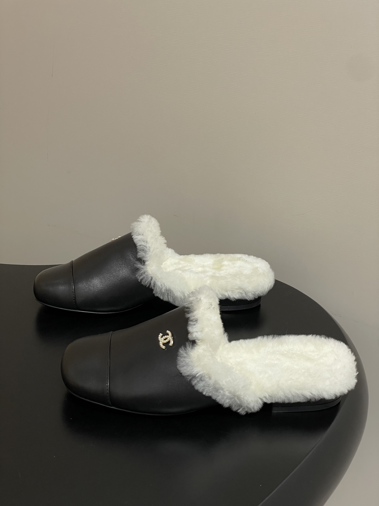 Pair of black leather mules with white shearling lining and gold interlocking logo on a black surface - Hình 3