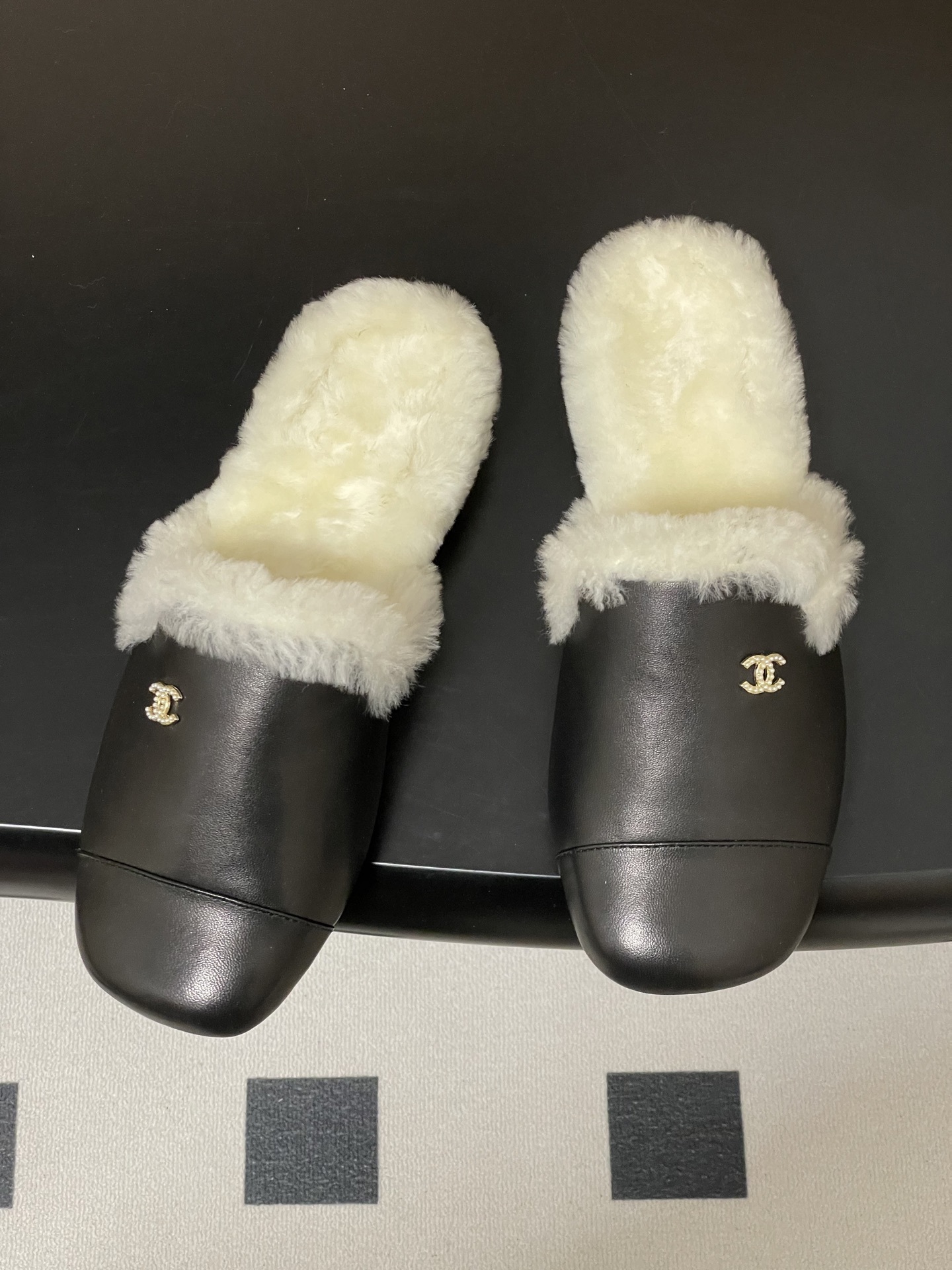Pair of black leather mules with white shearling lining and gold interlocking logo on a black surface - Hình 2