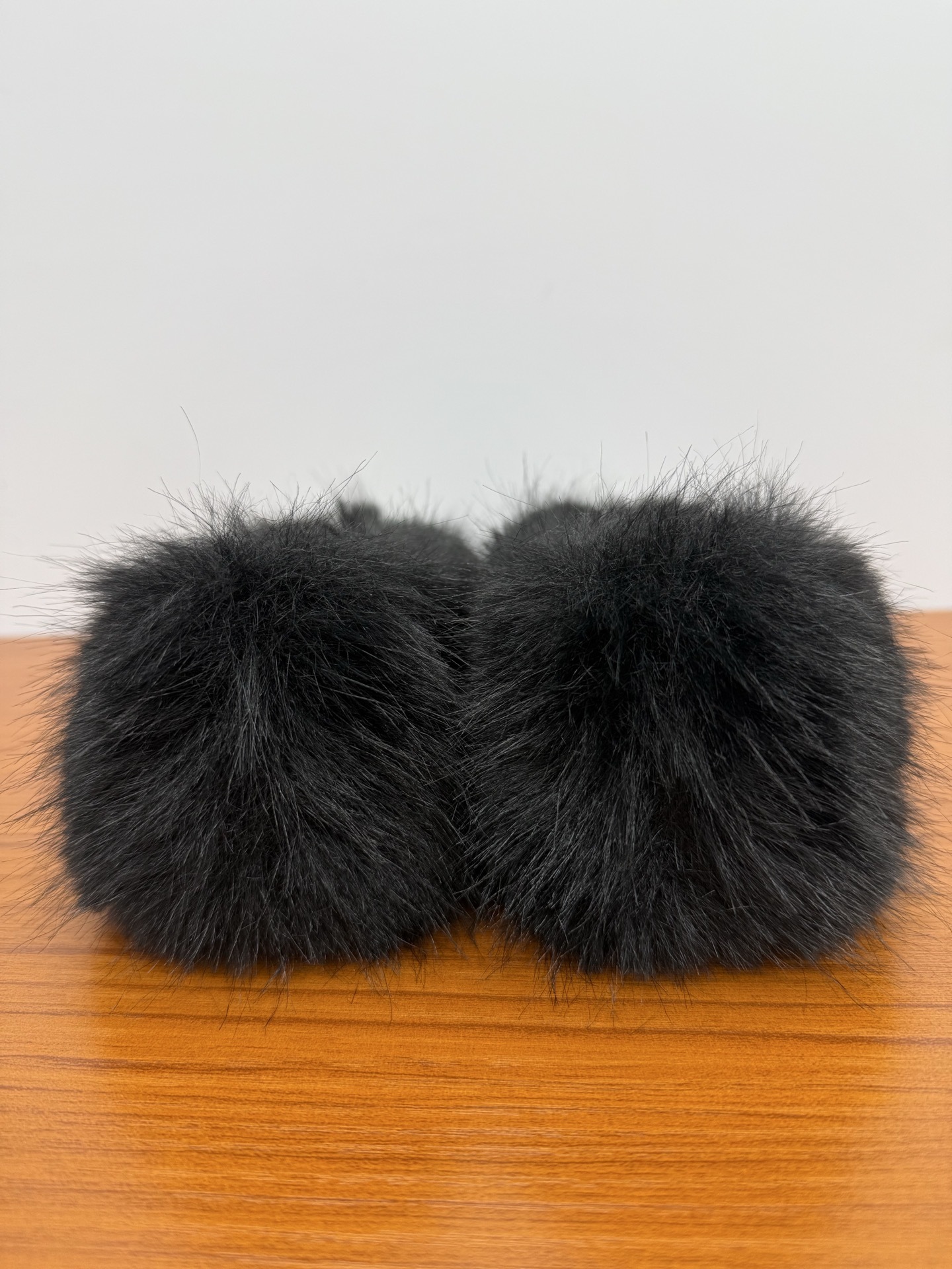Pair of black faux fur loafers with white pom-poms and crystal CC logos on a wooden table - Hình 8
