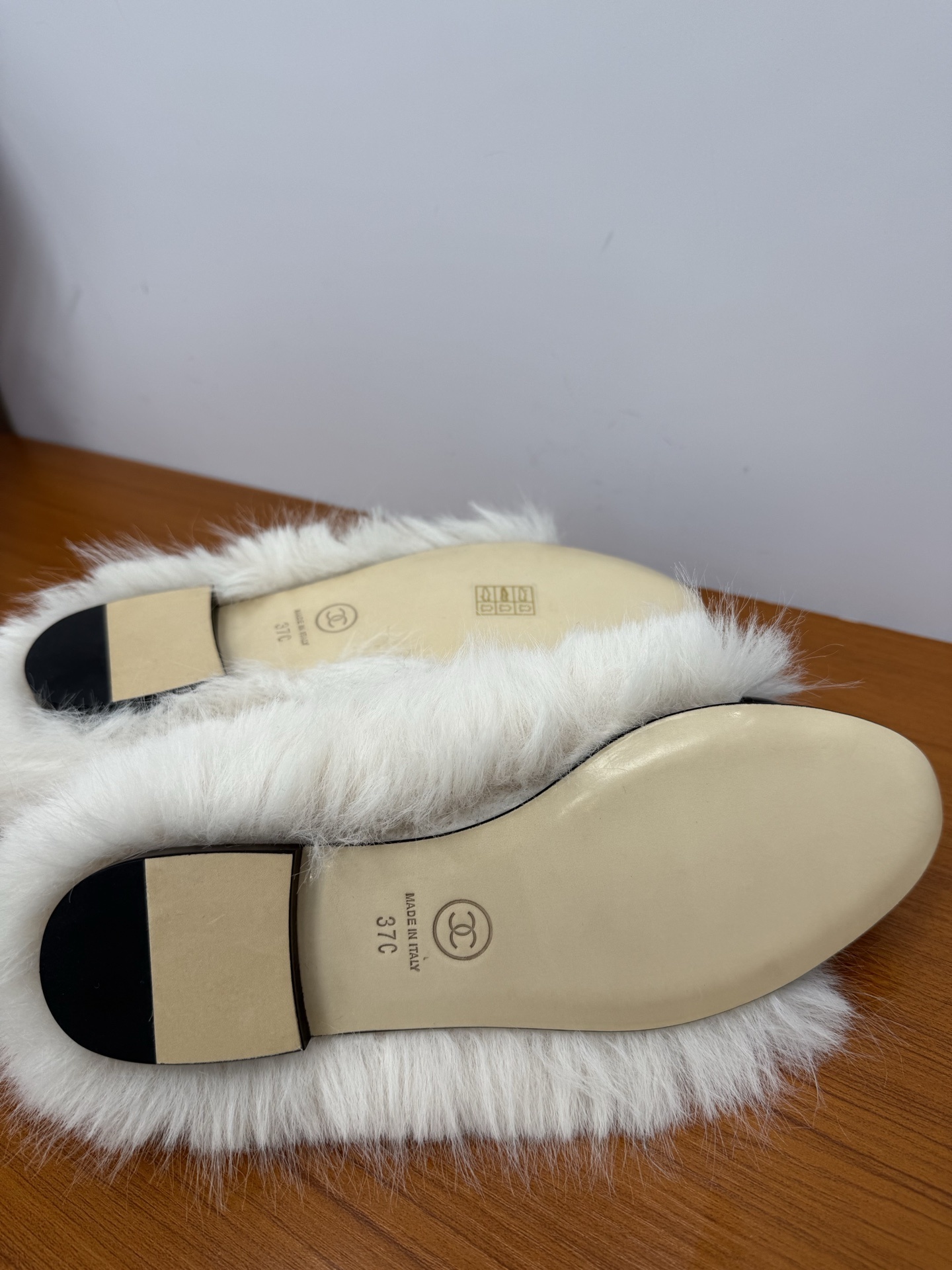 Pair of white faux fur slippers with black fur toe caps and silver crystal CC logos on a wooden surface - Hình 9