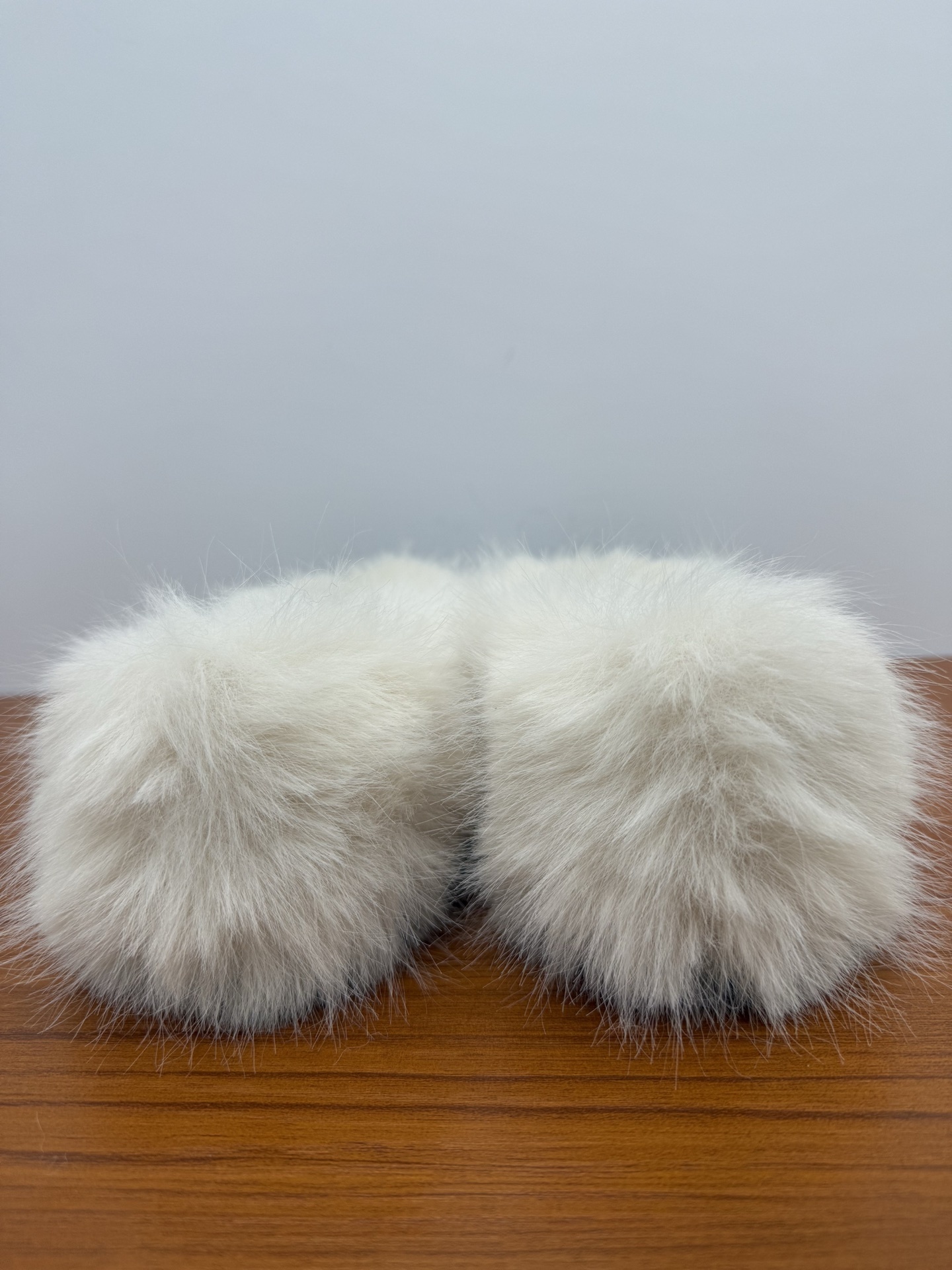 Pair of white faux fur slippers with black fur toe caps and silver crystal CC logos on a wooden surface - Hình 8