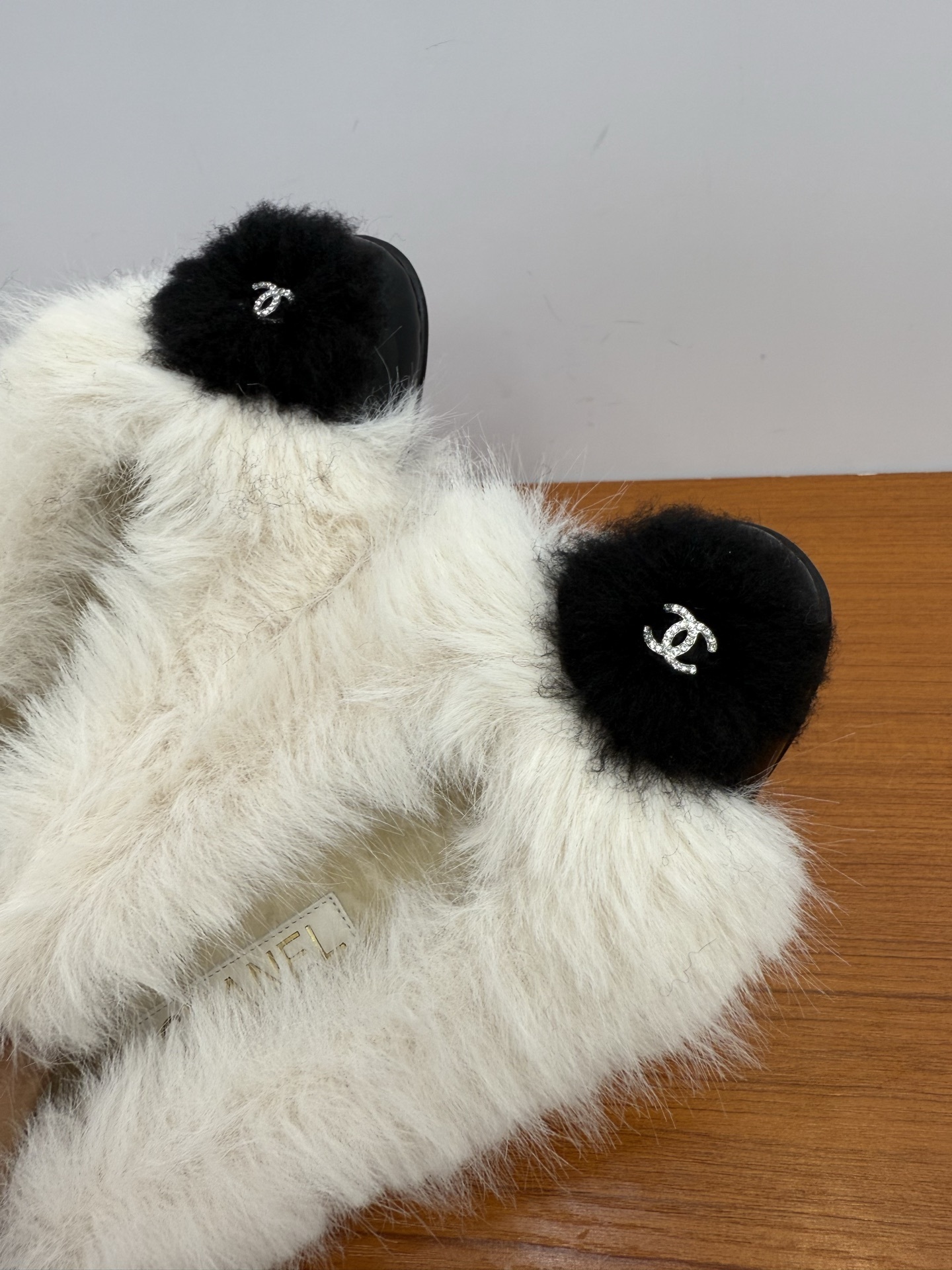Pair of white faux fur slippers with black fur toe caps and silver crystal CC logos on a wooden surface - Hình 7