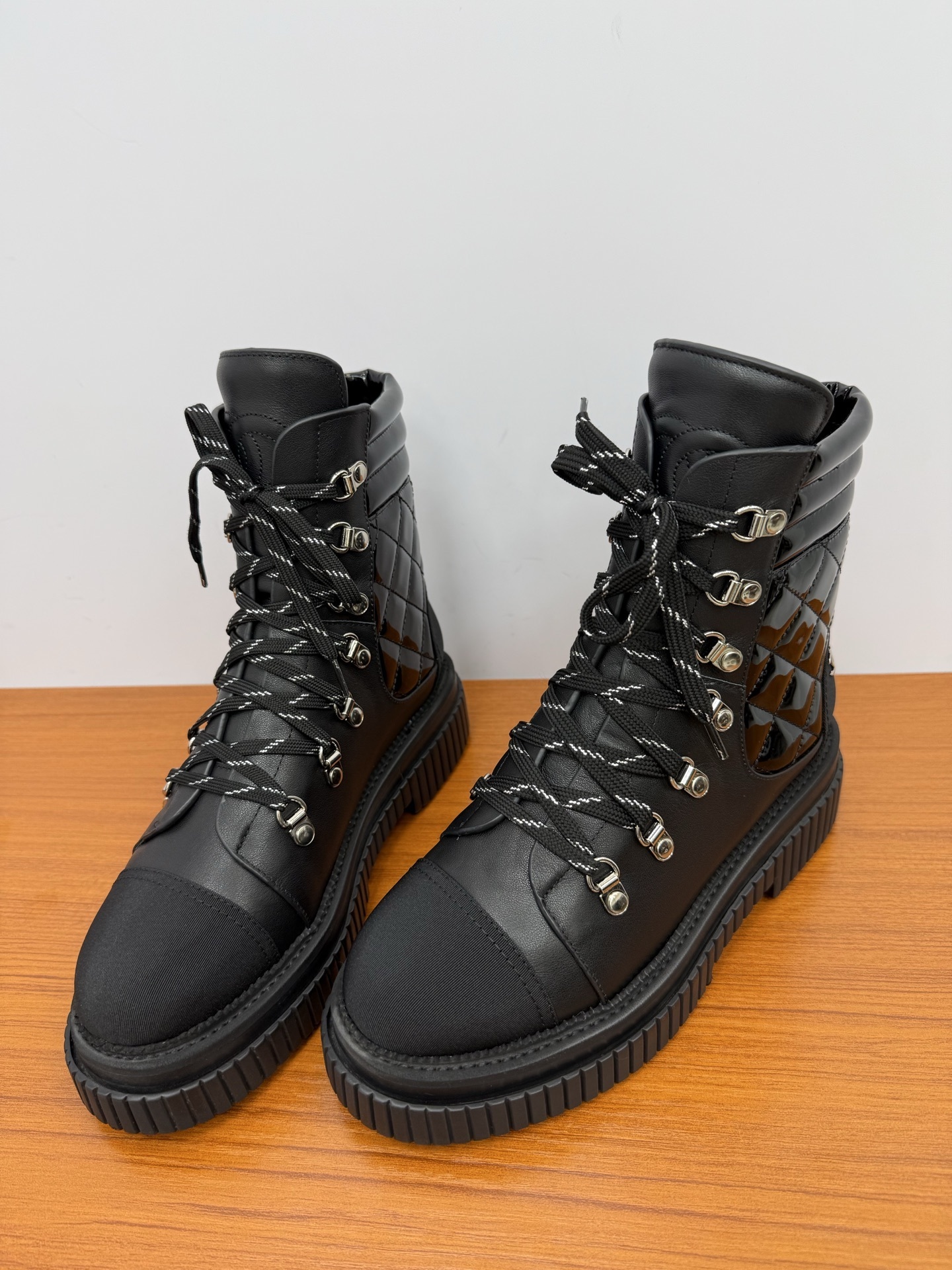 A pair of women's black leather lace-up combat boots with platform lug soles and quilted patent side panels on a wooden surface. - Hình 6